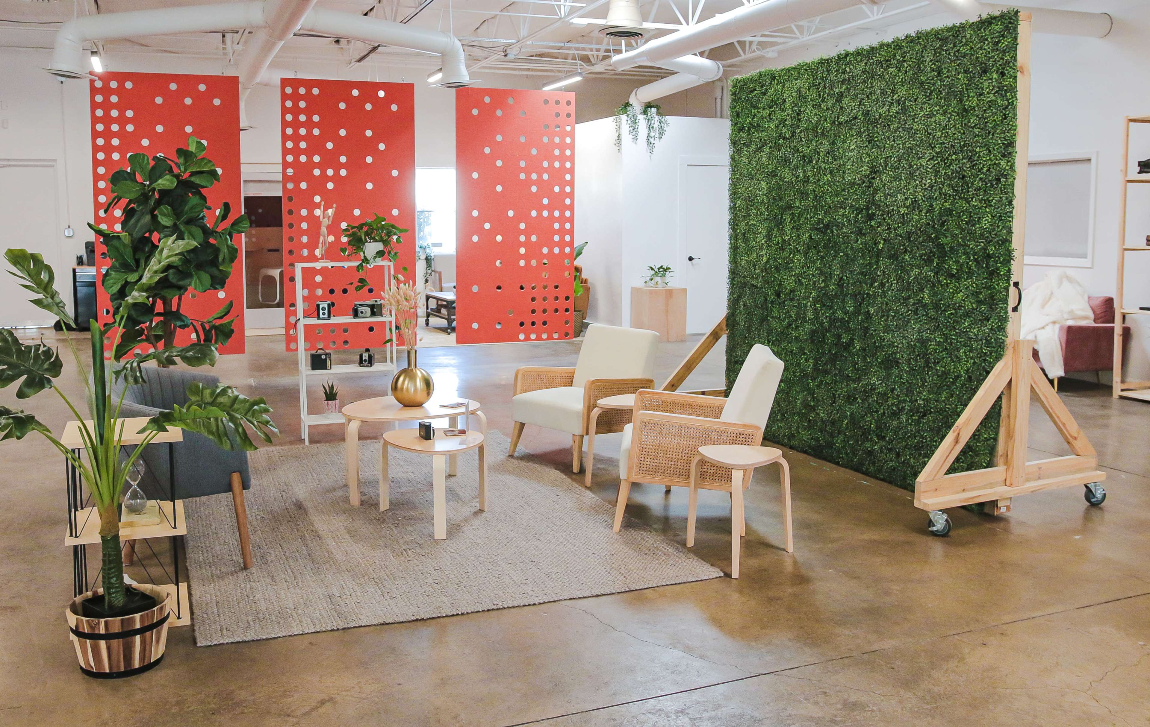 A modern interior space featuring a seating area with two armchairs and a coffee table, surrounded by greenery and decorative elements against a backdrop of red dotted walls.