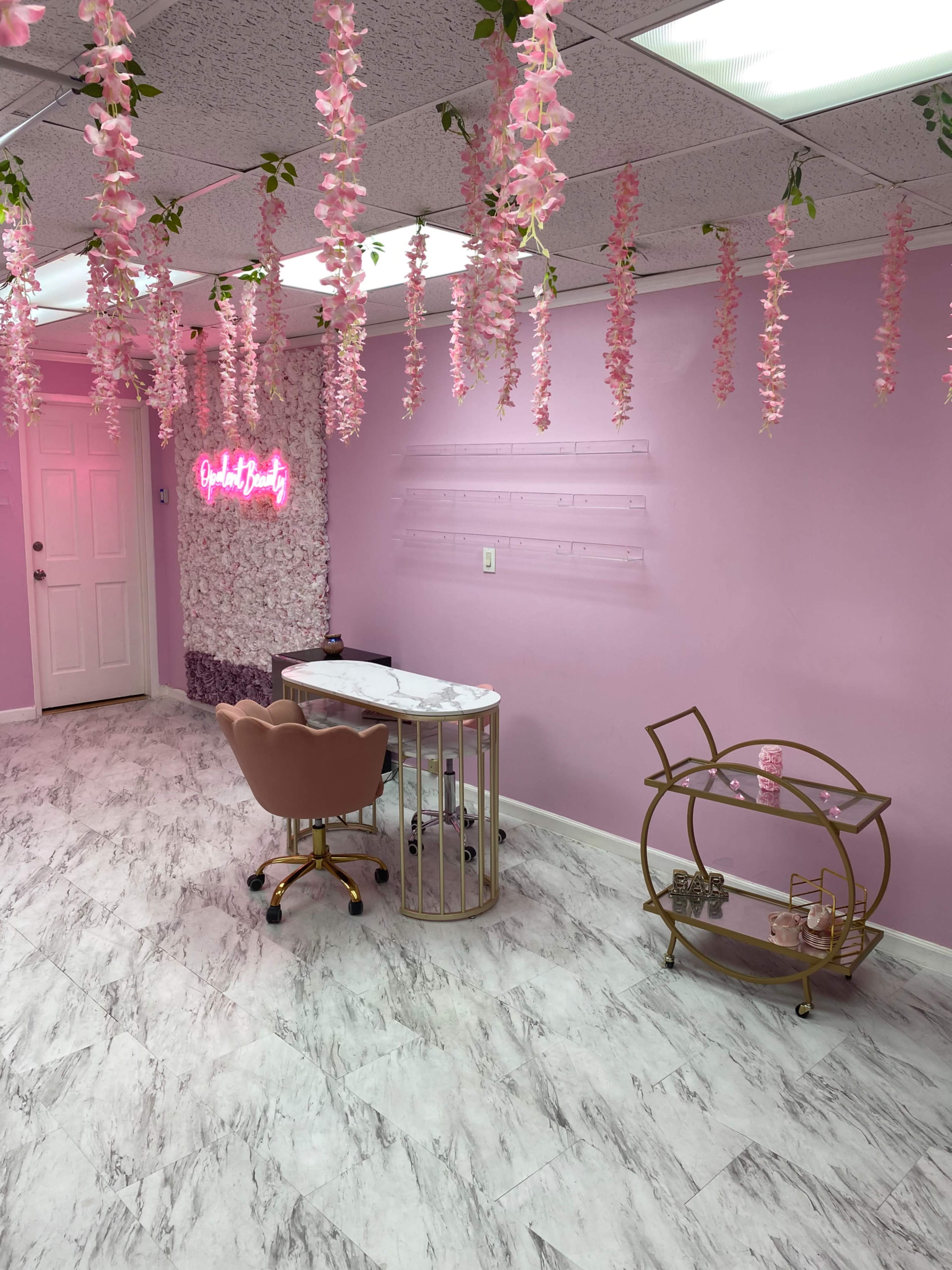 A salon interior with pink walls, a marble topped desk, a chair, and decorative faux flowers hanging from the ceiling.