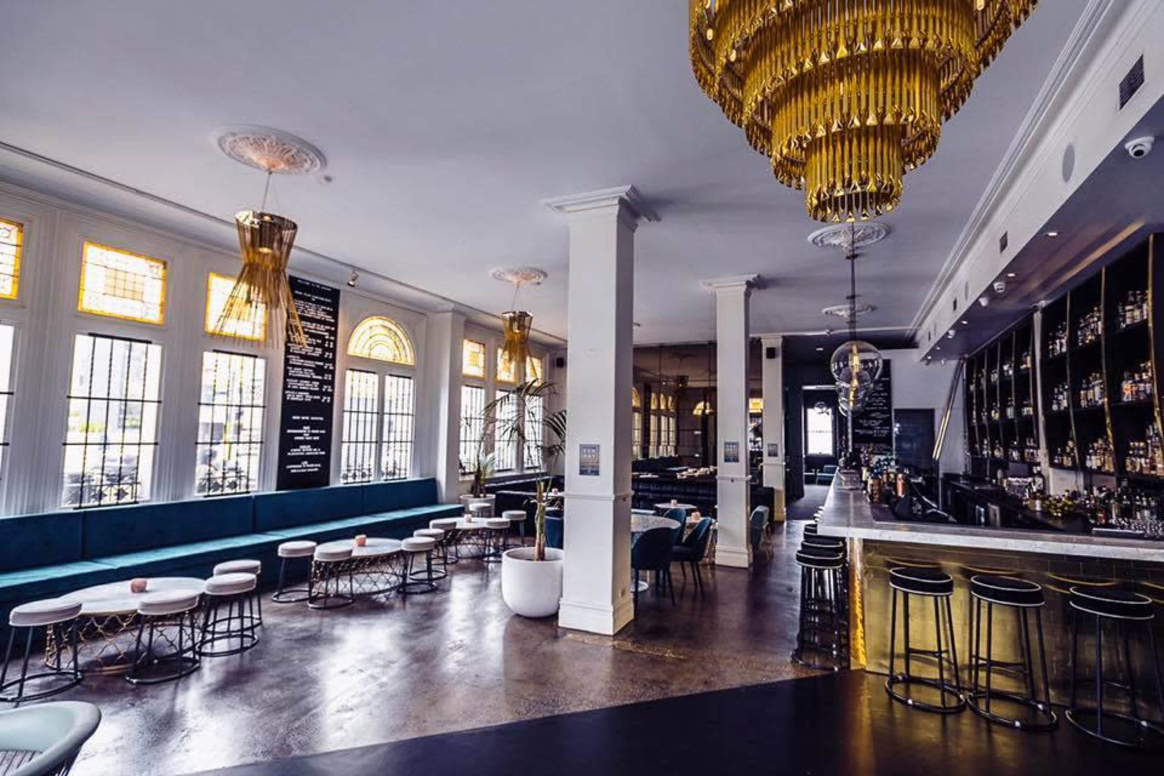 A spacious bar and lounge area featuring a modern design with golden chandeliers, plush seating, and a sleek bar counter.