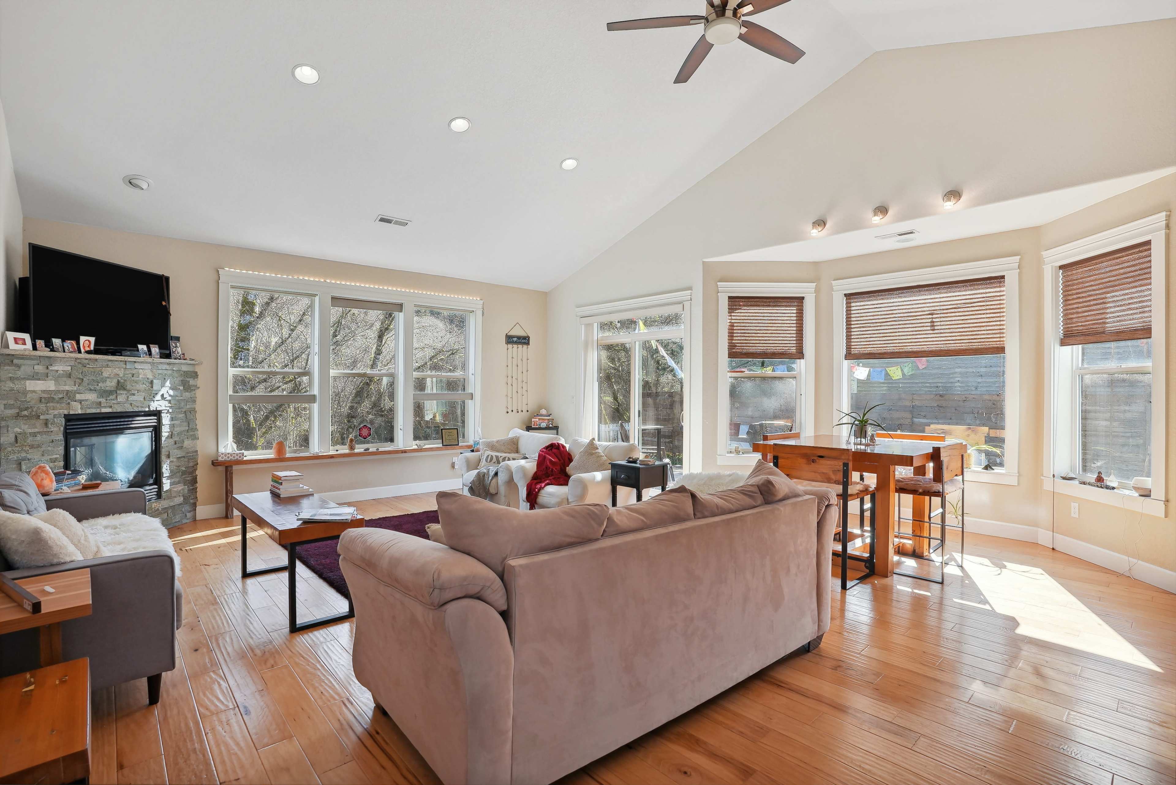 A spacious living room with large windows, a stone fireplace, and a comfortable seating arrangement.