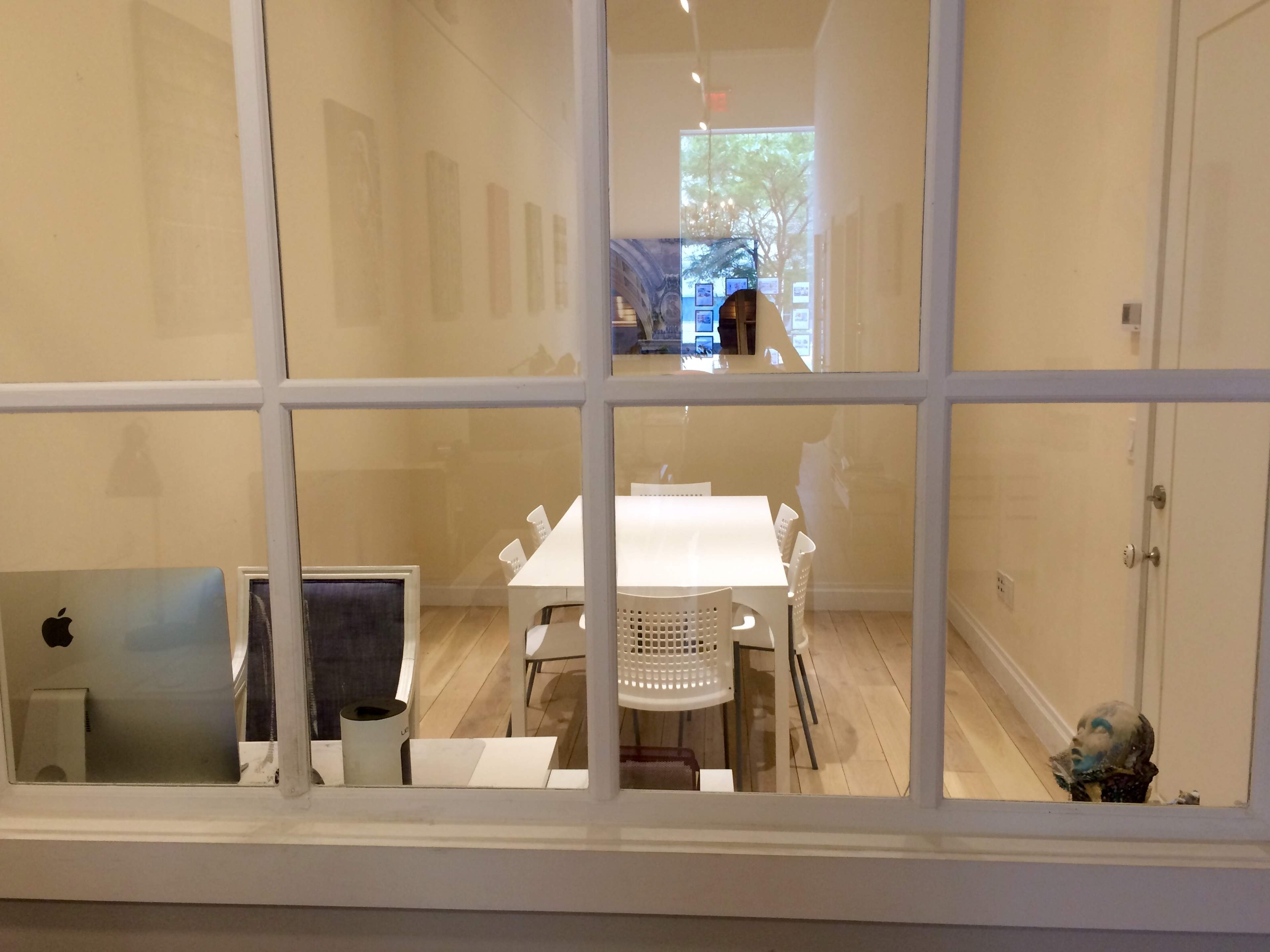 A bright meeting room with a long white table surrounded by chairs, visible through a window.