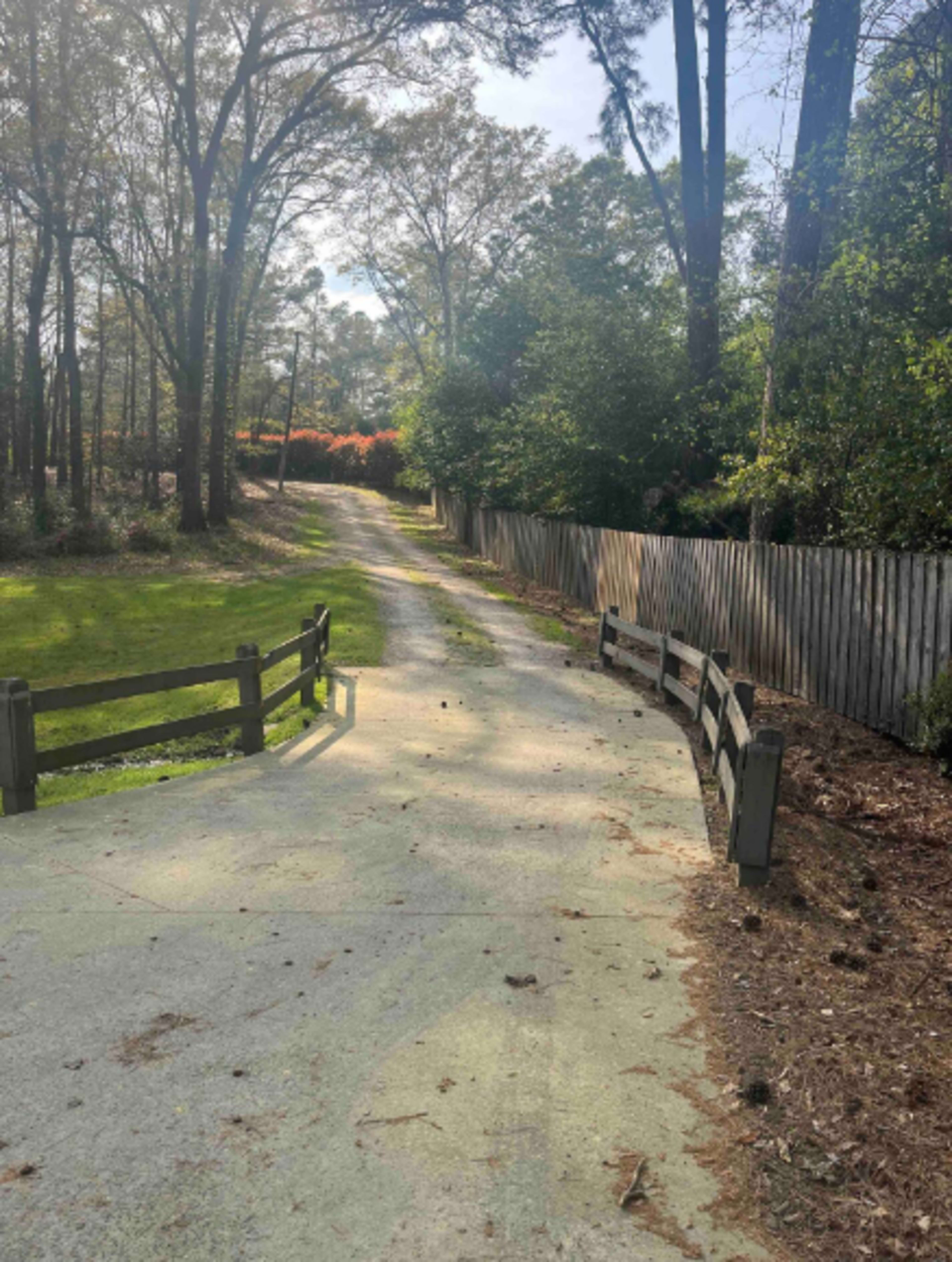 A gravel path winds through a wooded area, bordered by a wooden fence and flanked by greenery on either side.