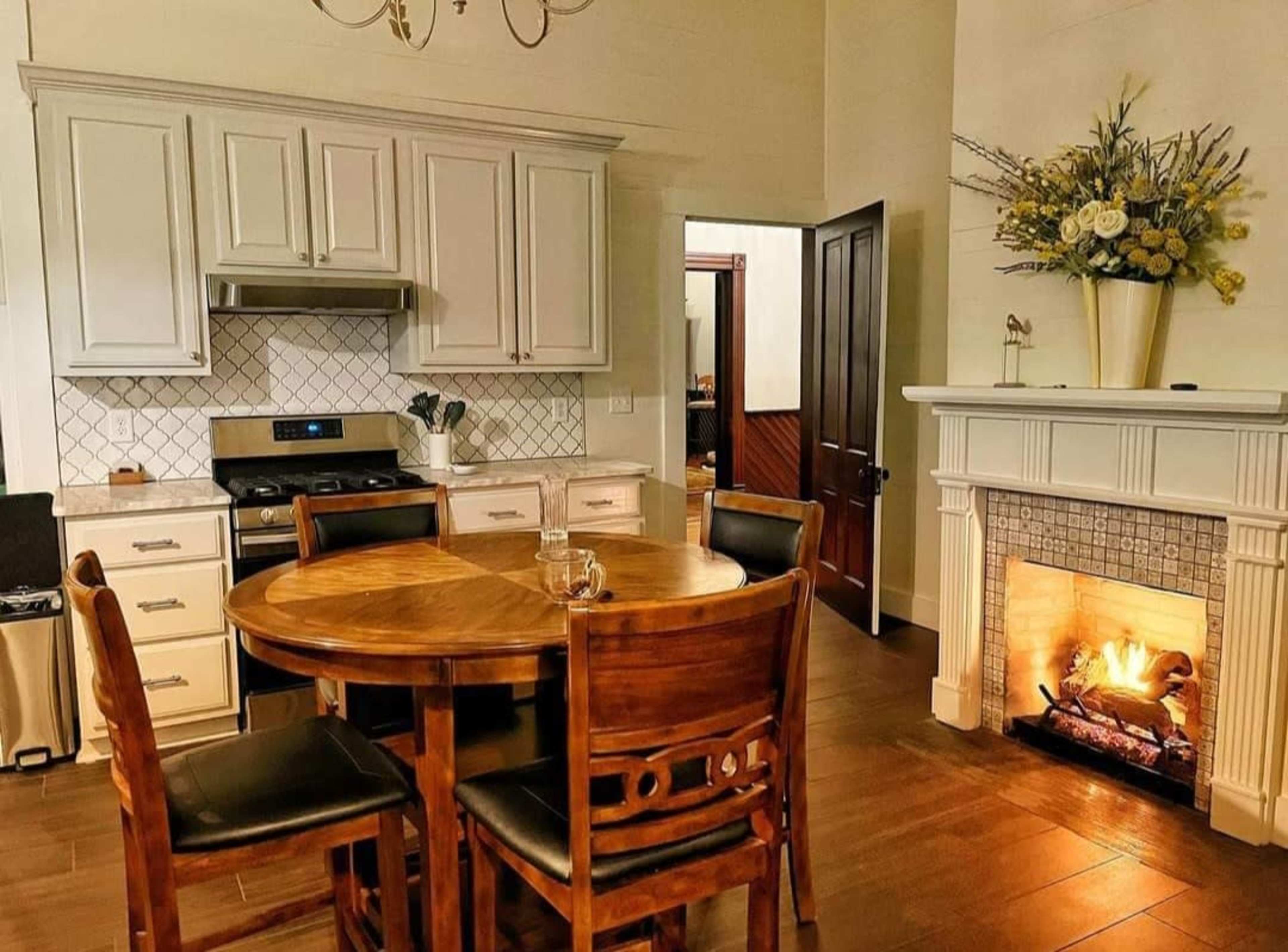 A kitchen with a round wooden table and chairs, featuring a fireplace and equipped with white cabinetry and modern appliances.