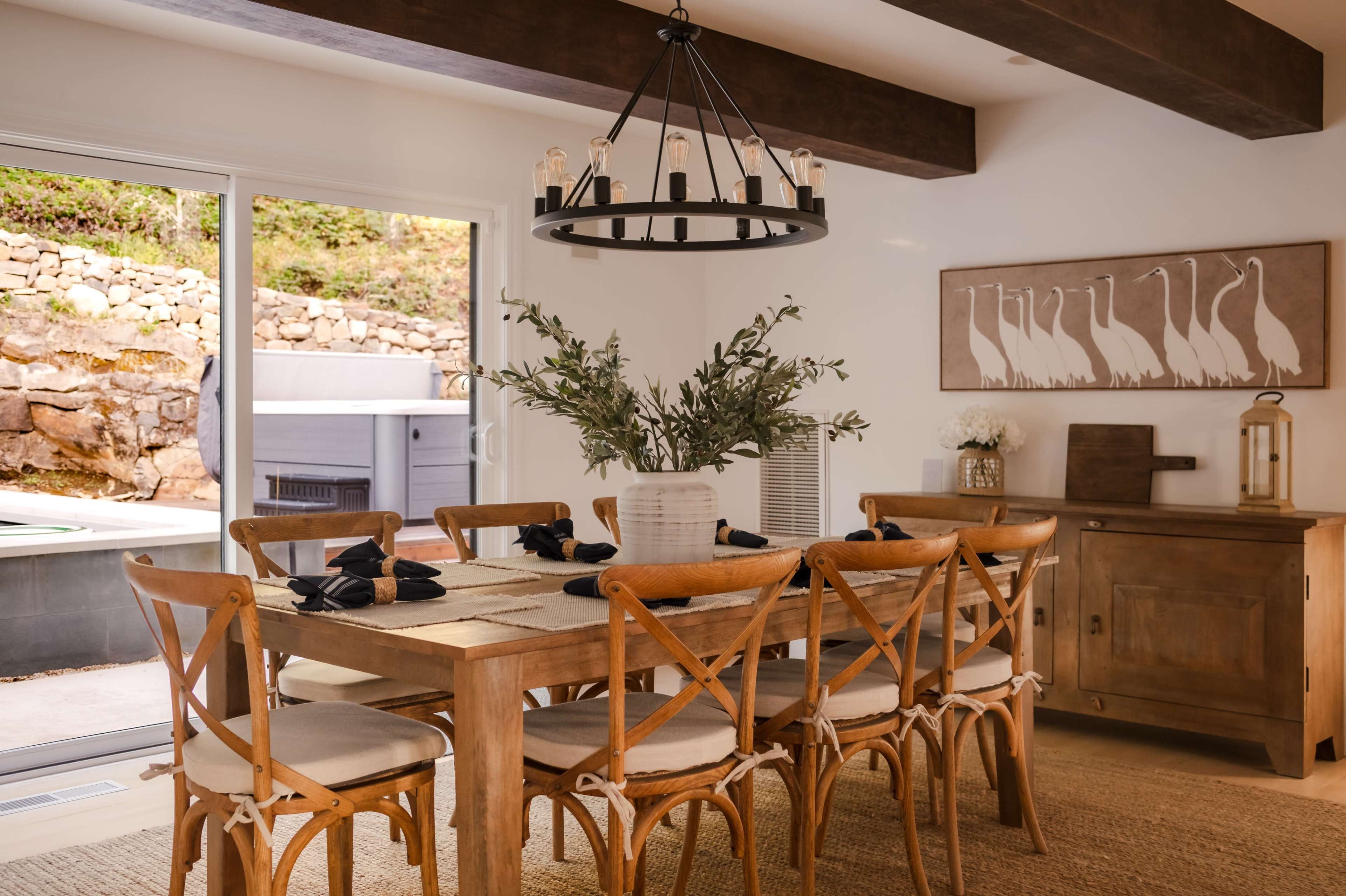 The image shows a modern dining room with a large wooden table surrounded by chairs, a pendant light above, and a sideboard against the wall.