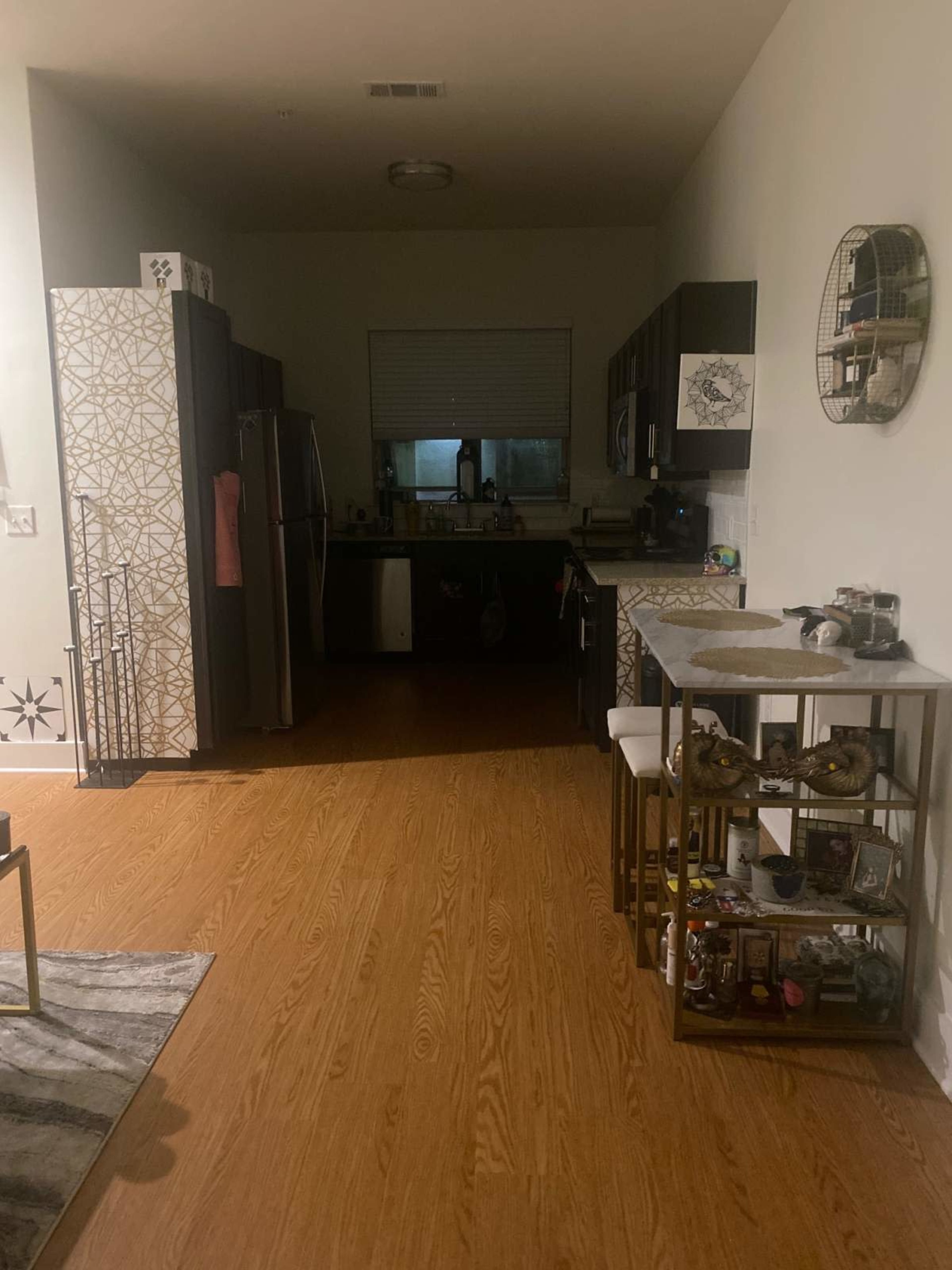 The image shows a kitchen area with modern cabinets, a stainless steel refrigerator, and a dining table displaying various decorative items.