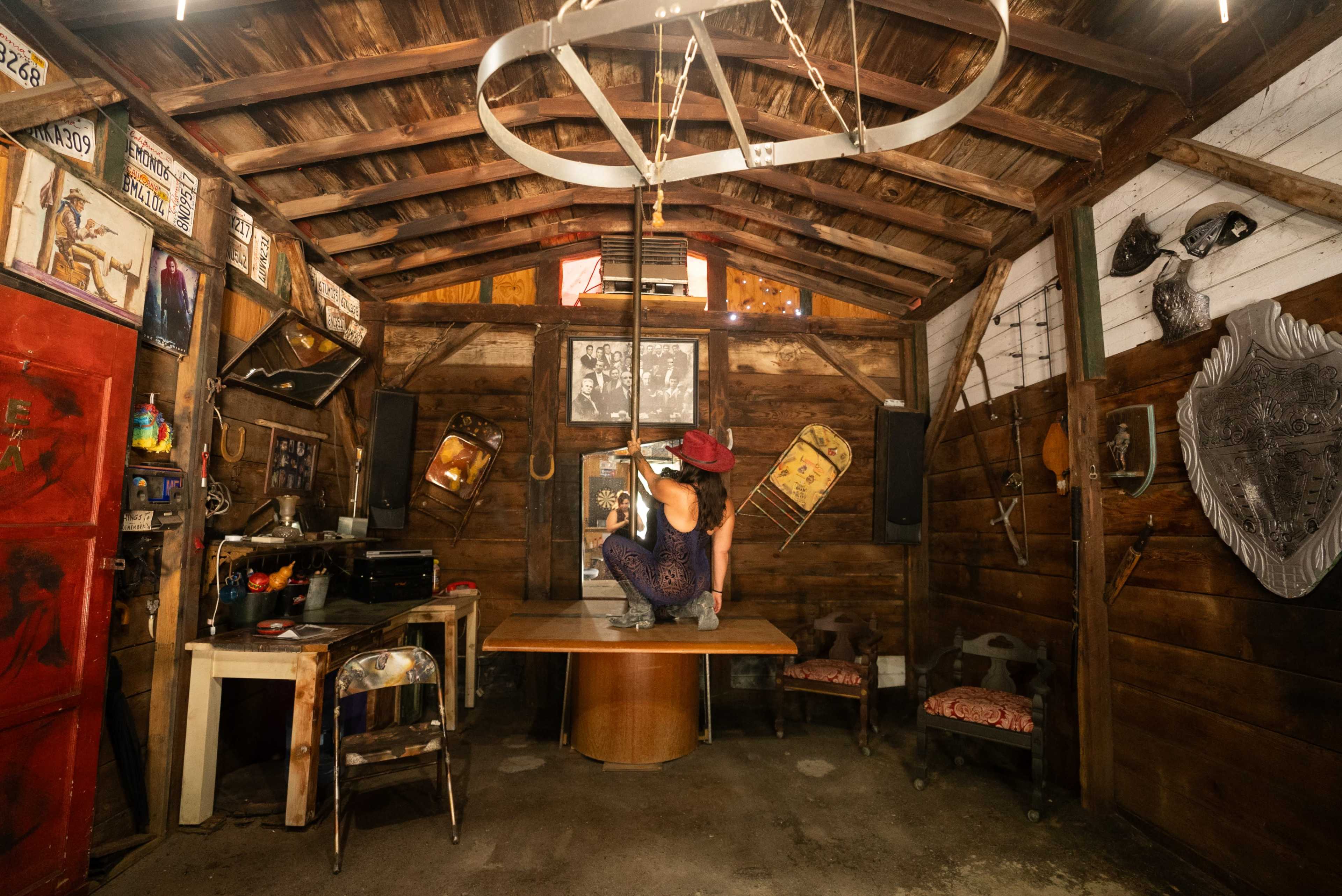 A person is sitting on a round table in a rustic wooden room decorated with vintage posters and tools.