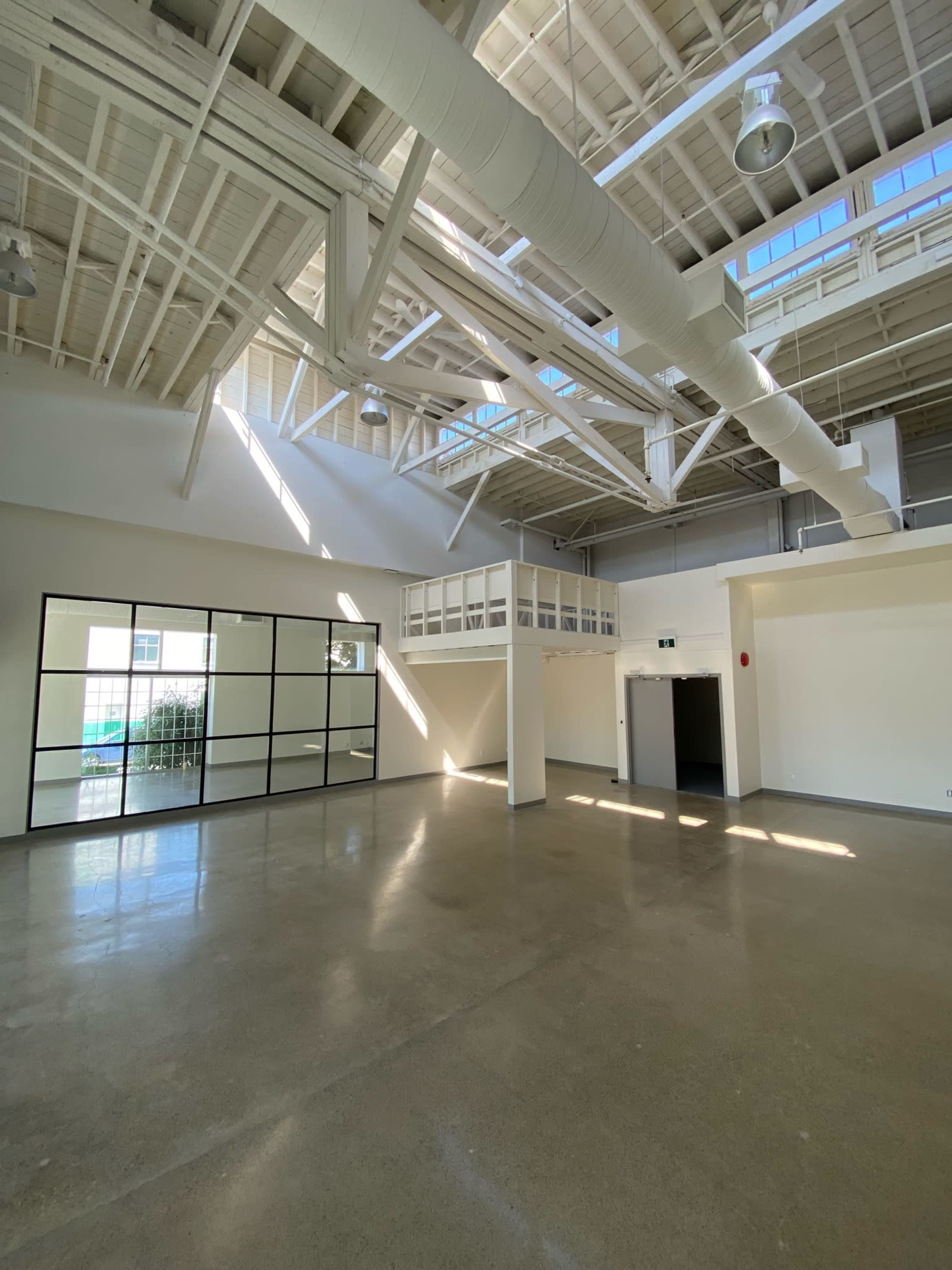 A spacious, empty interior with high ceilings, large windows, and polished concrete floors.
