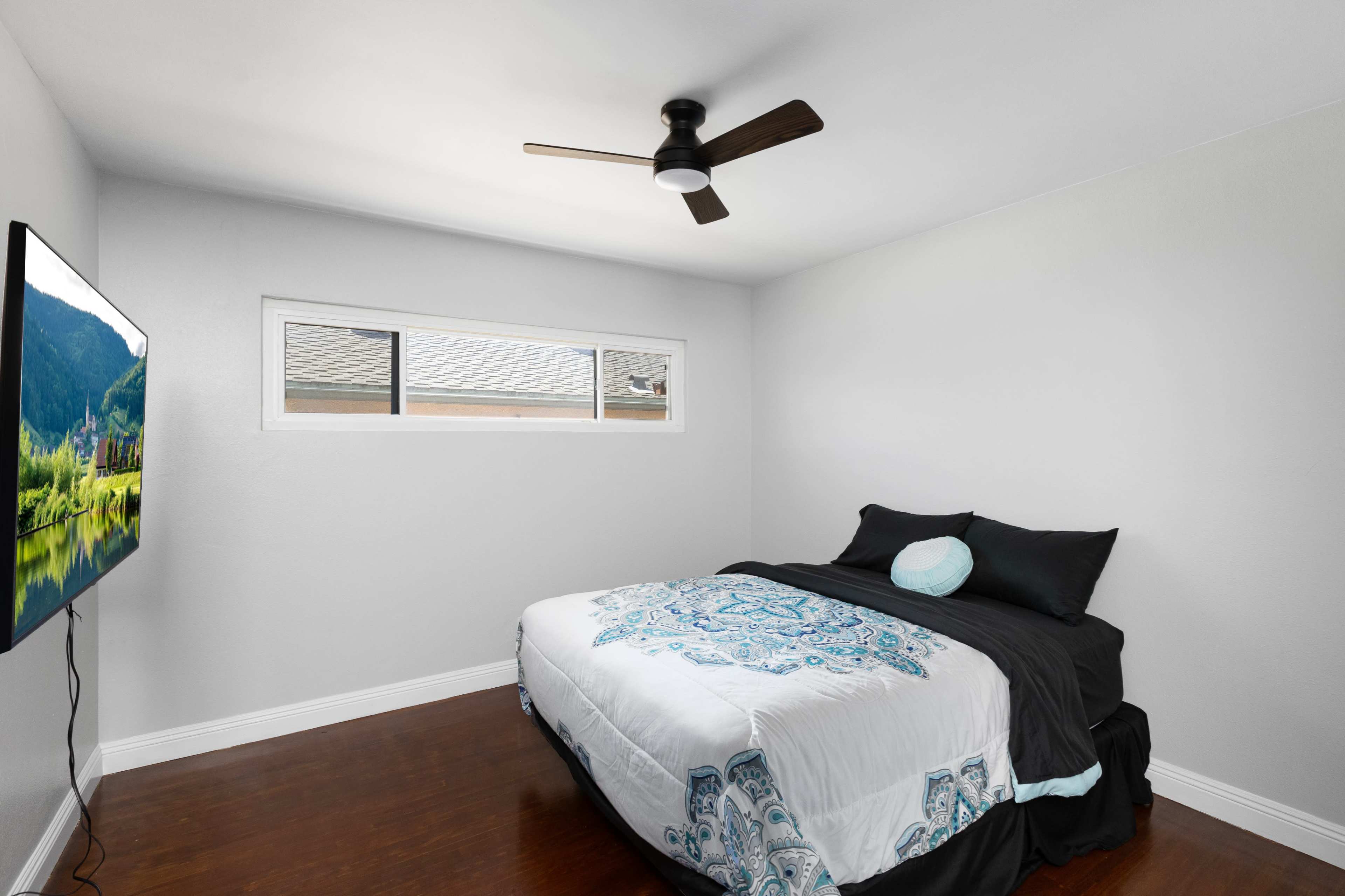 The room features a bed with a patterned comforter, a ceiling fan, and a wall-mounted television.