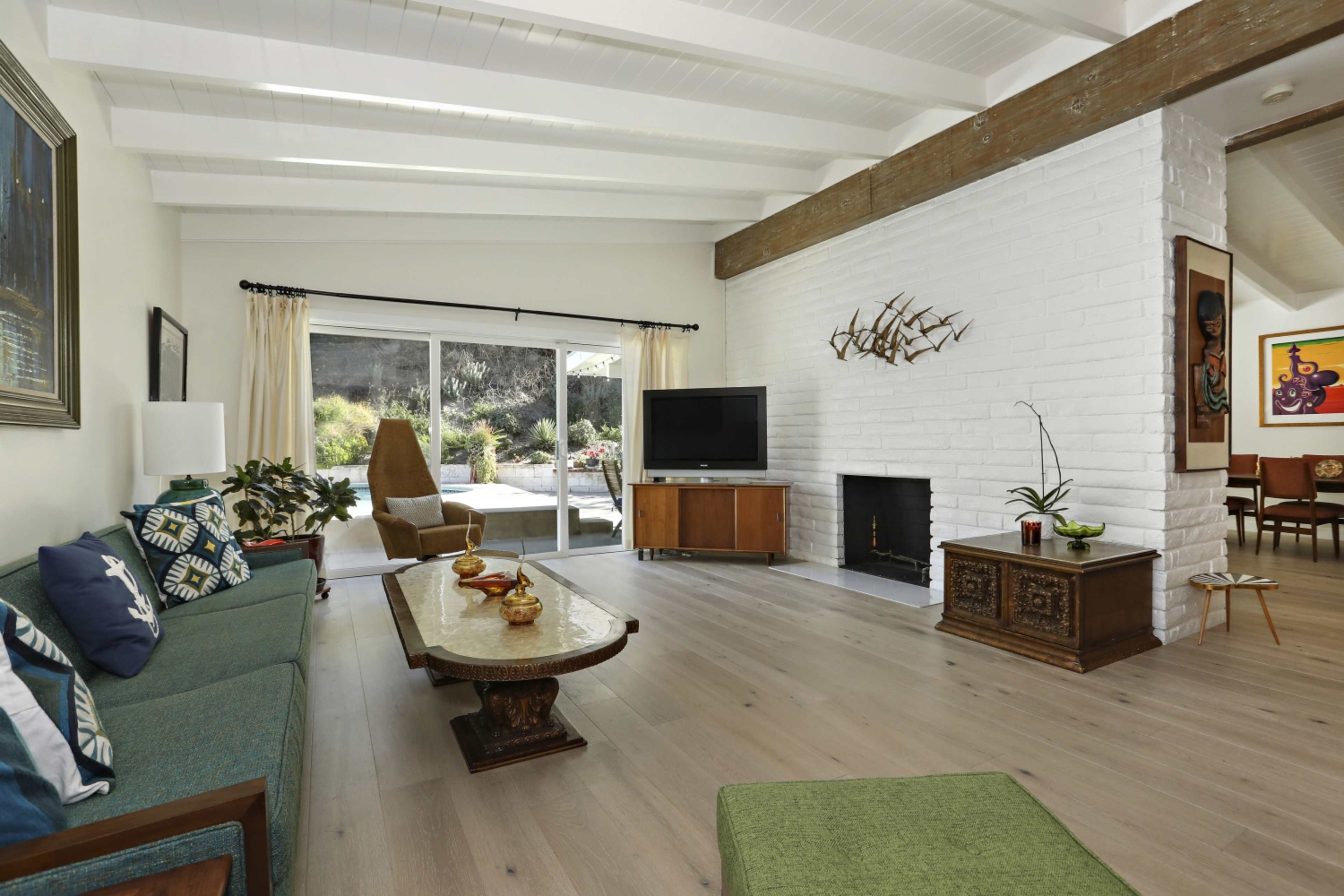 The living room features a spacious layout with a light color palette, a large window, a fireplace, and modern furniture.