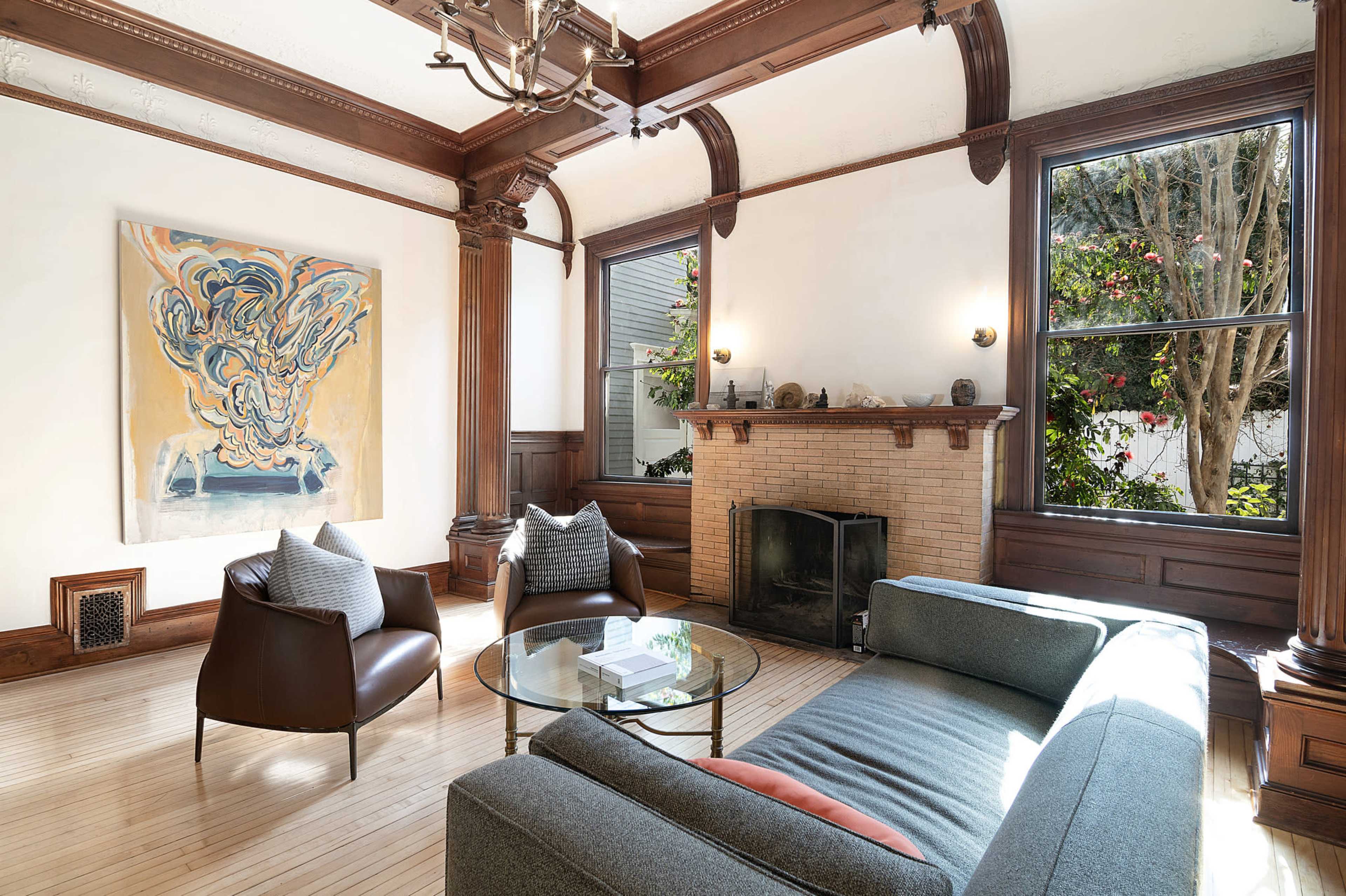 The image depicts a well-lit living room featuring a modern sofa, a glass coffee table, and a decorative fireplace with a piece of artwork on the wall.