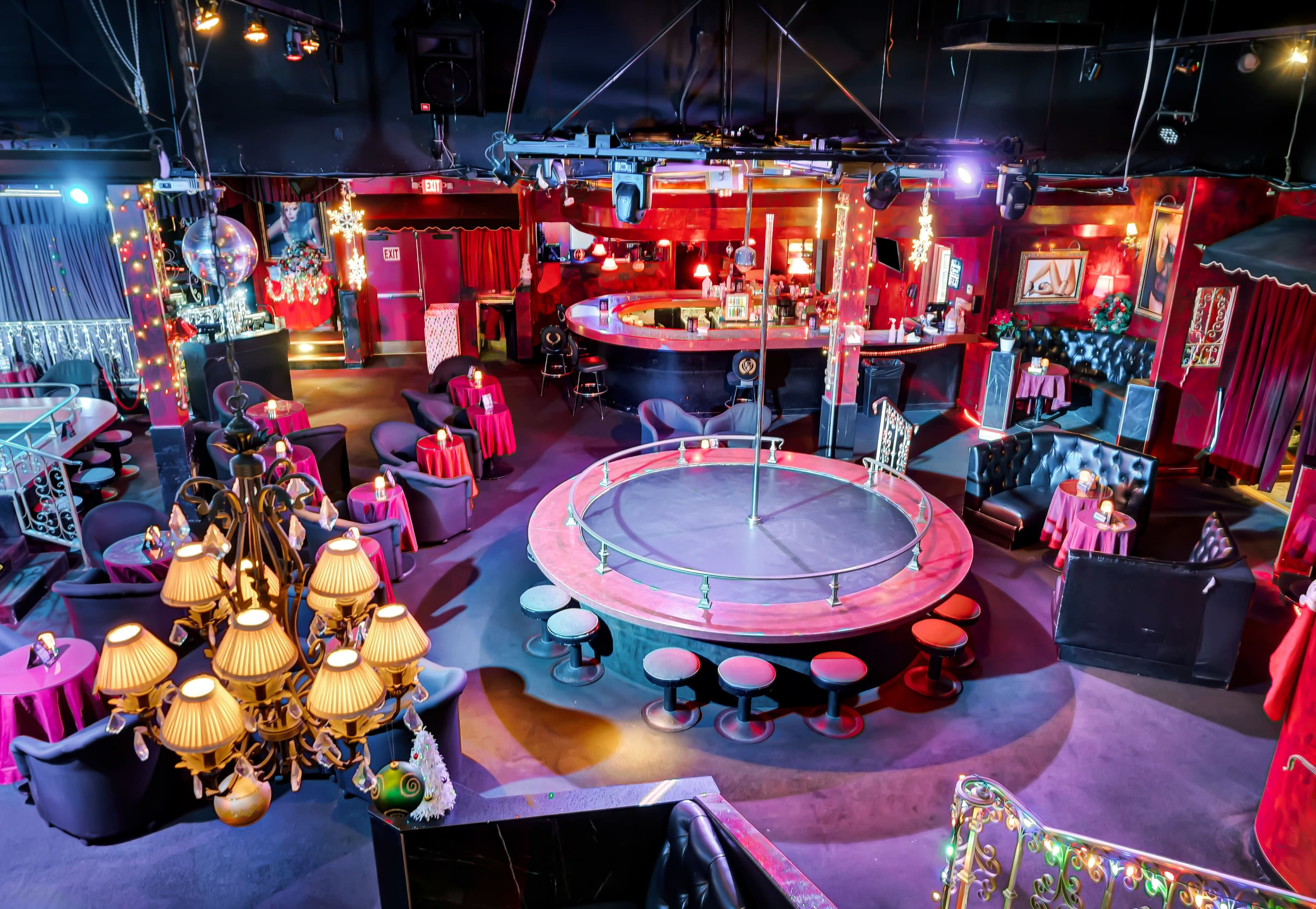 The image shows a dimly lit entertainment venue with a circular stage at the center, surrounded by seating areas decorated with red and black furnishings.