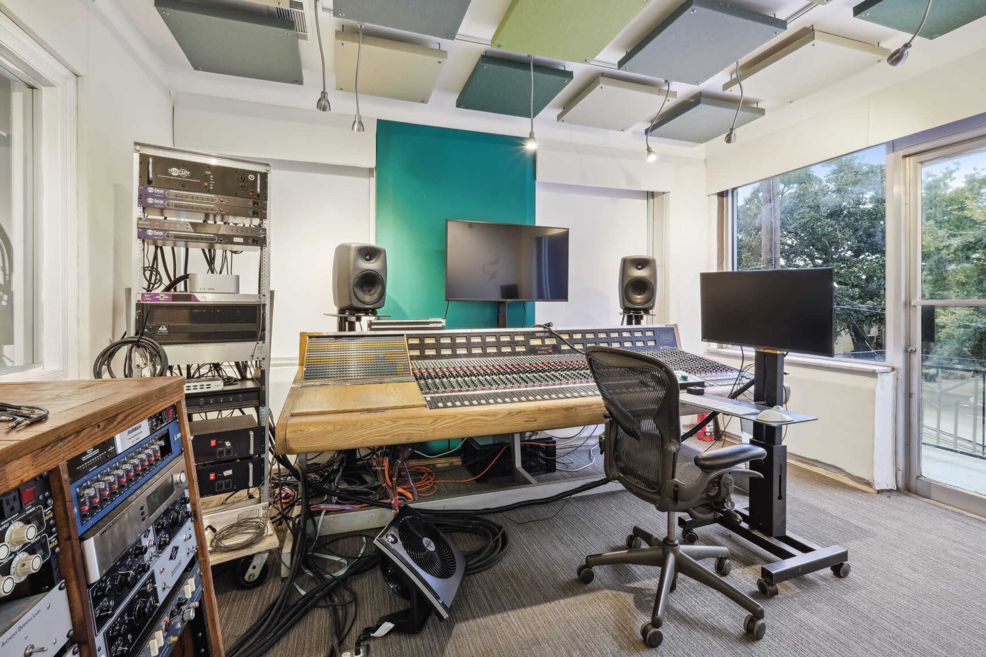 A recording studio features a large audio mixing console surrounded by sound equipment and monitors.