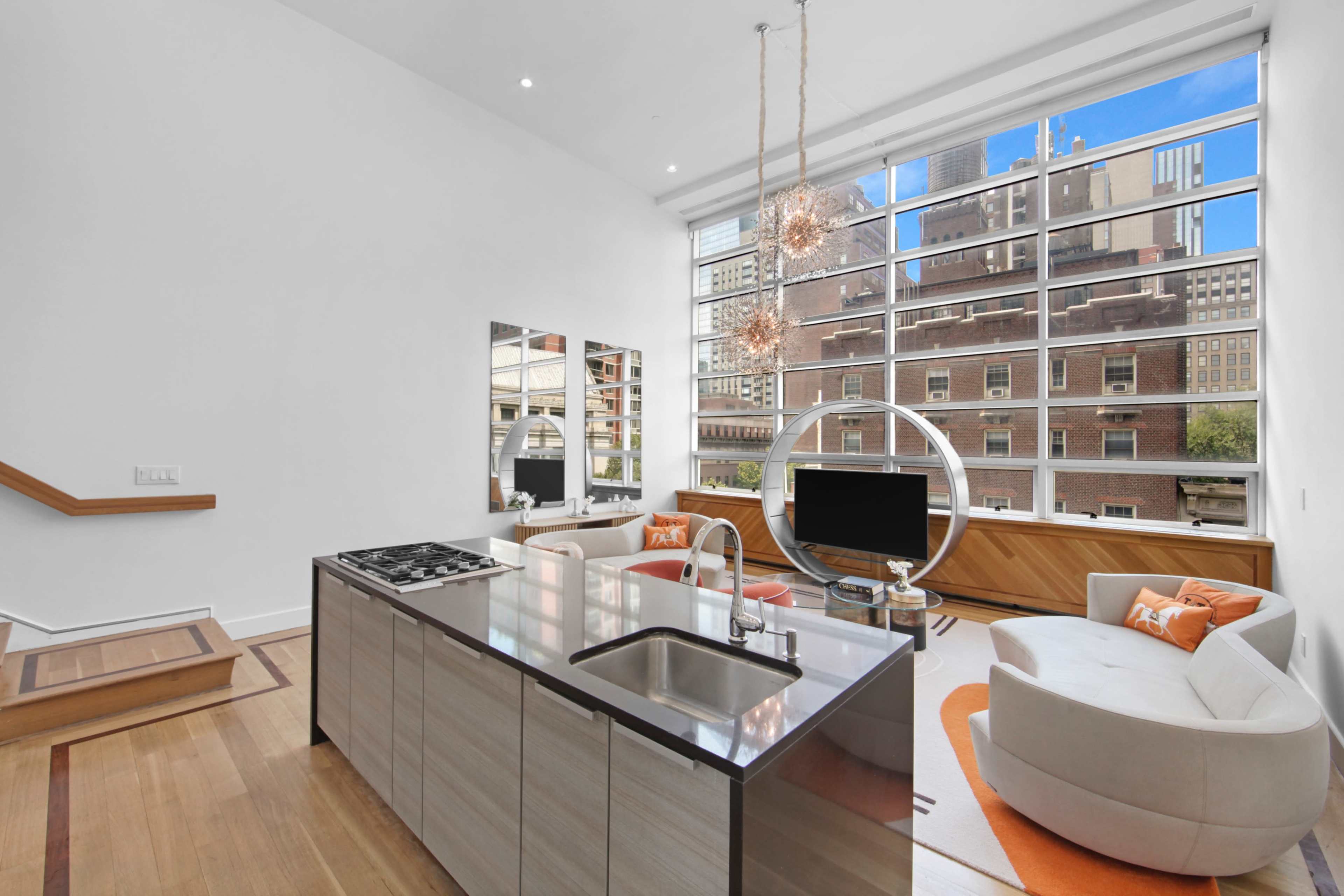 The image shows a modern living space with a kitchen island, a circular lounge chair, and large windows overlooking a cityscape.