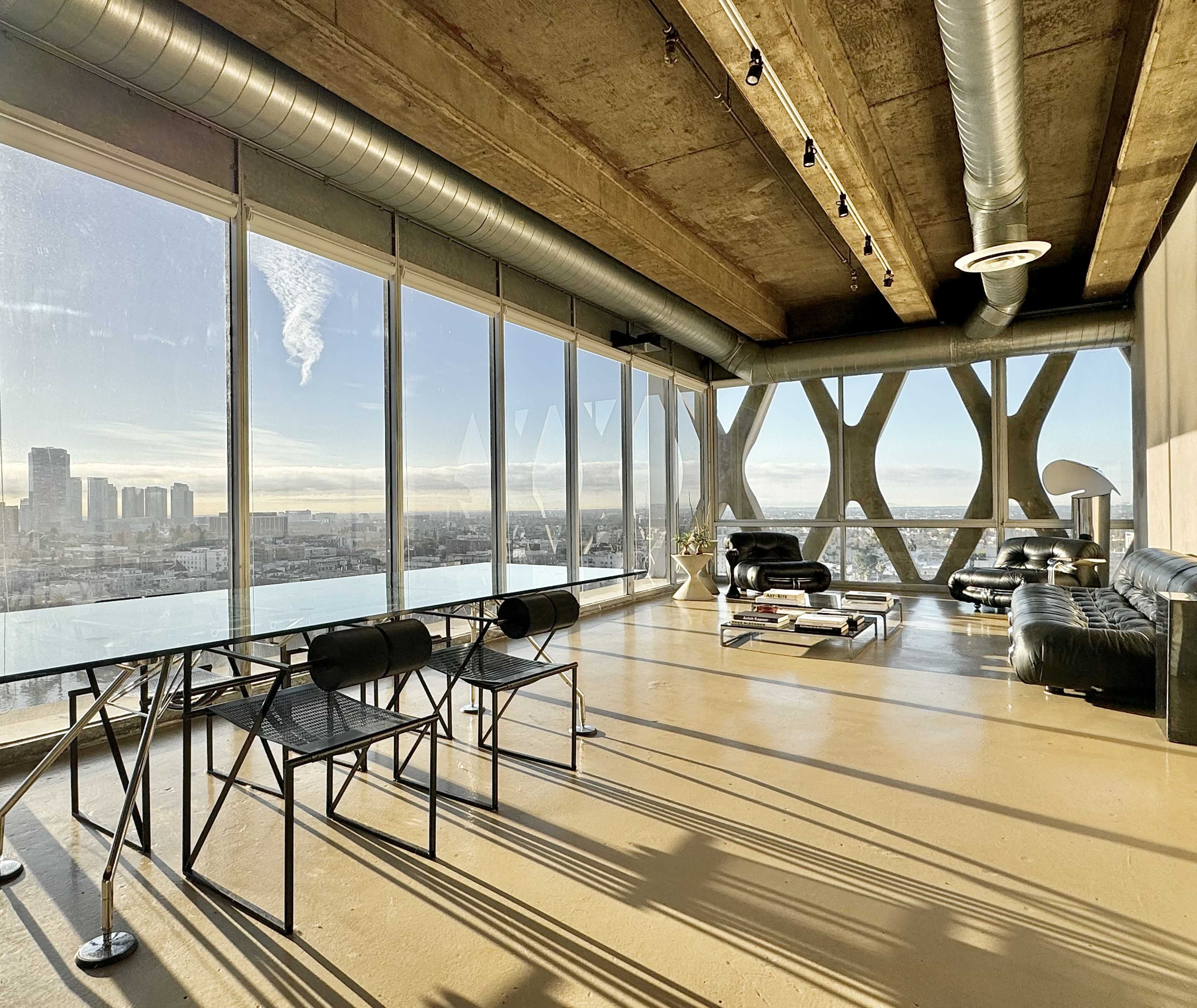 A modern, industrial-style living space with large windows offering a view of a city skyline.