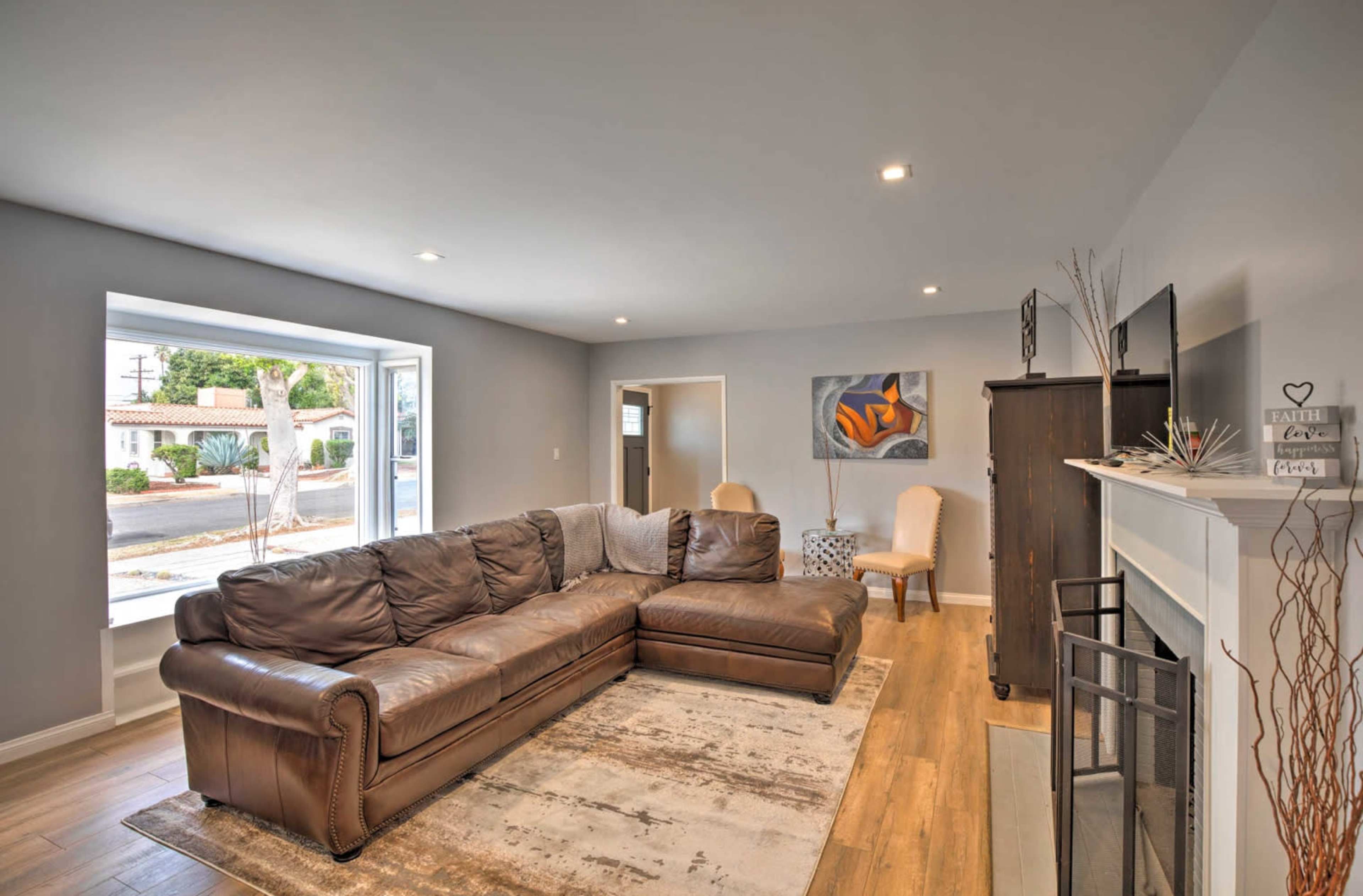 The image shows a modern living room with a large brown sectional sofa, a fireplace, and a window facing the street.