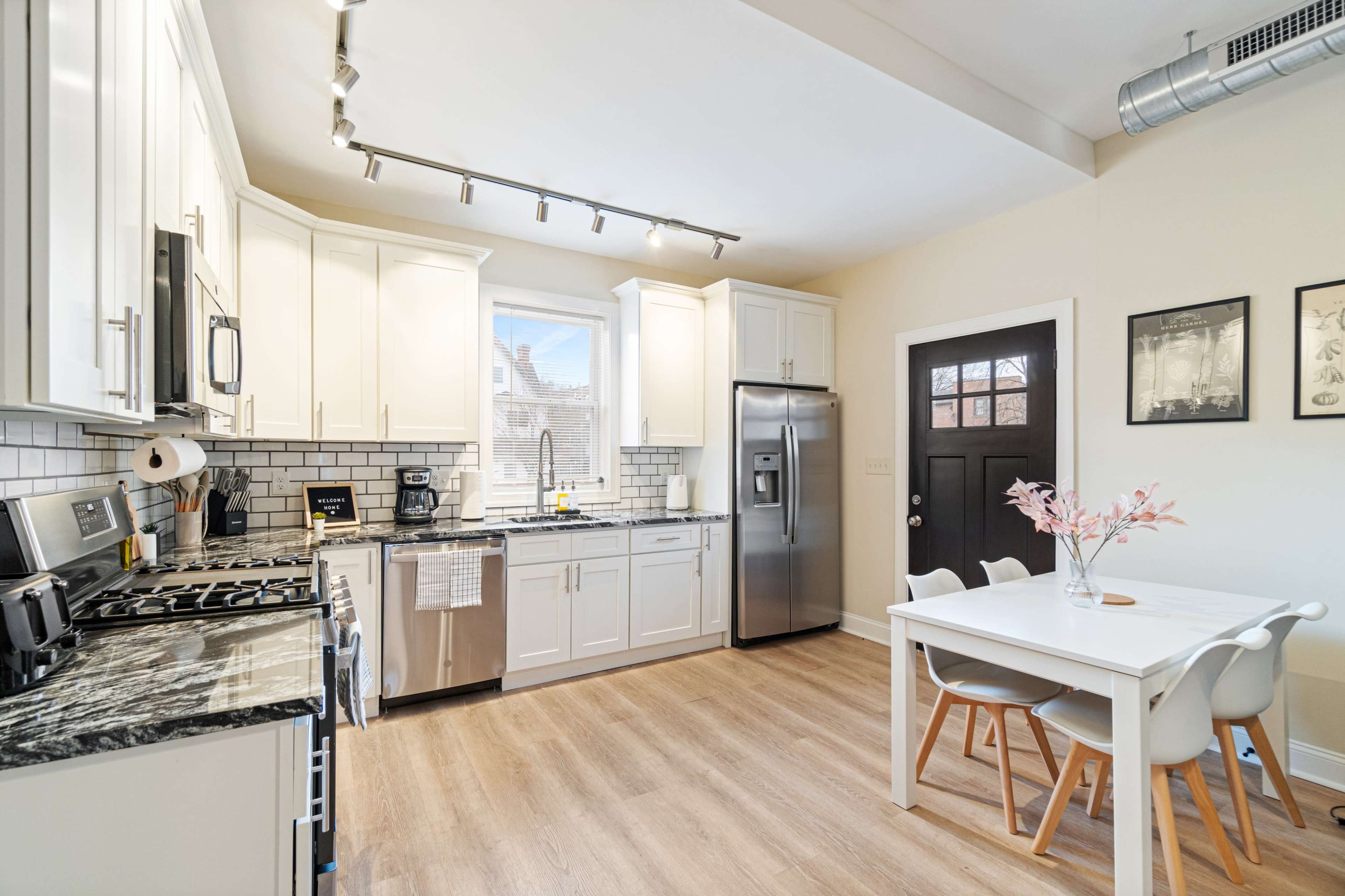 The image shows a modern kitchen with white cabinets, stainless steel appliances, and a dining table set for four.