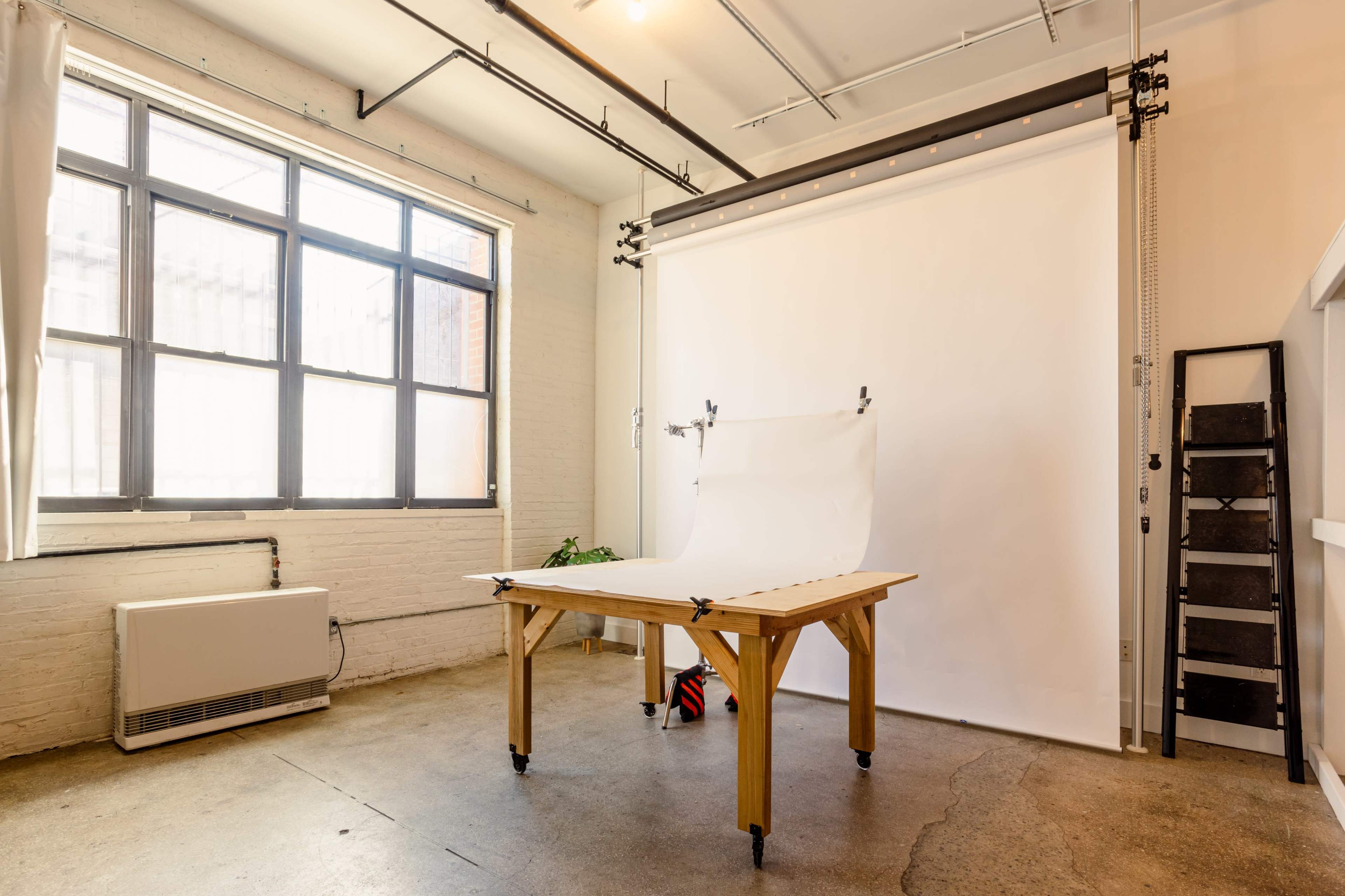 A photography studio featuring a wooden table in front of a backdrop and a large window.