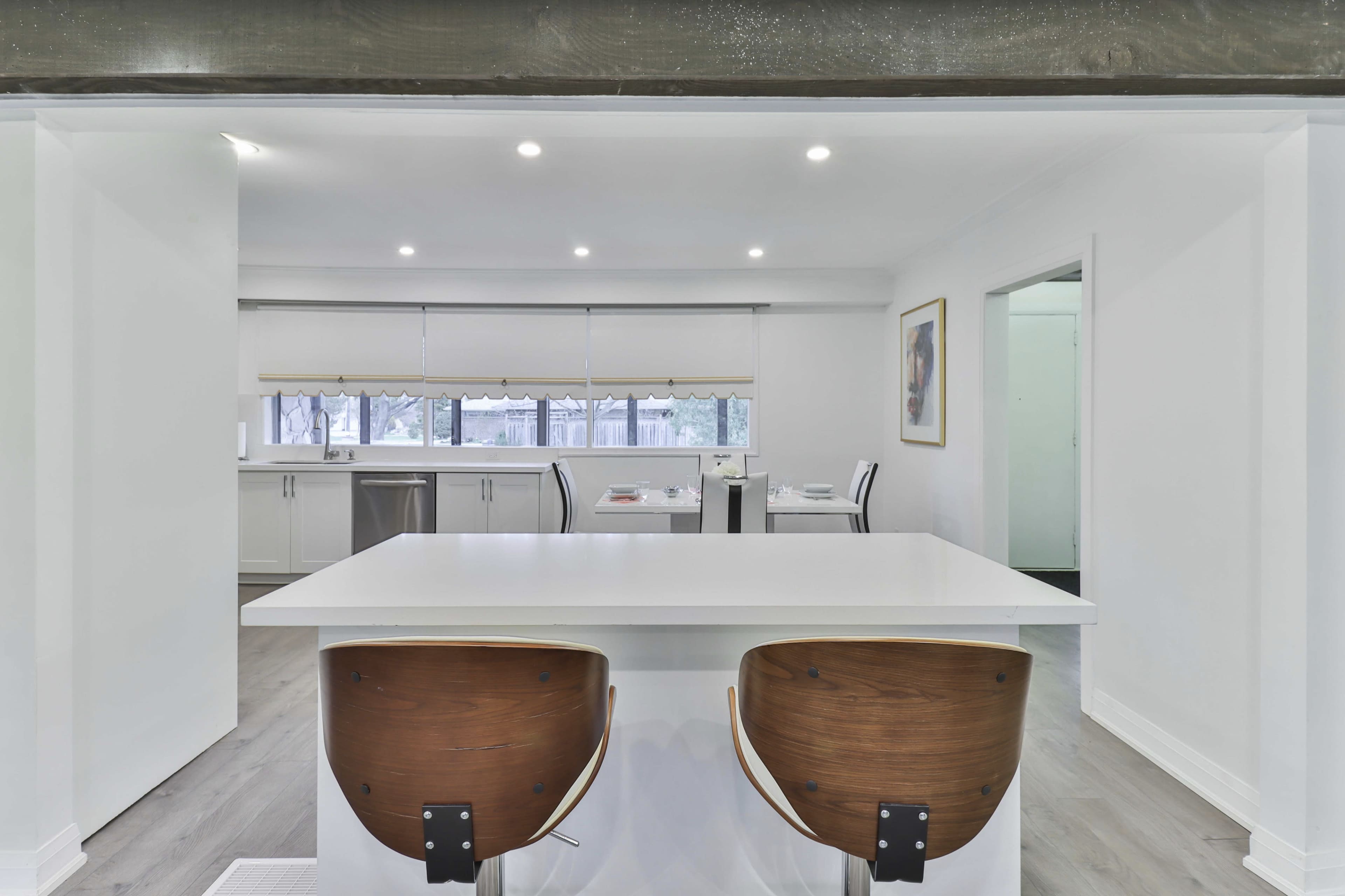 A modern kitchen features a white island with two wooden bar stools, illuminated by recessed lighting.