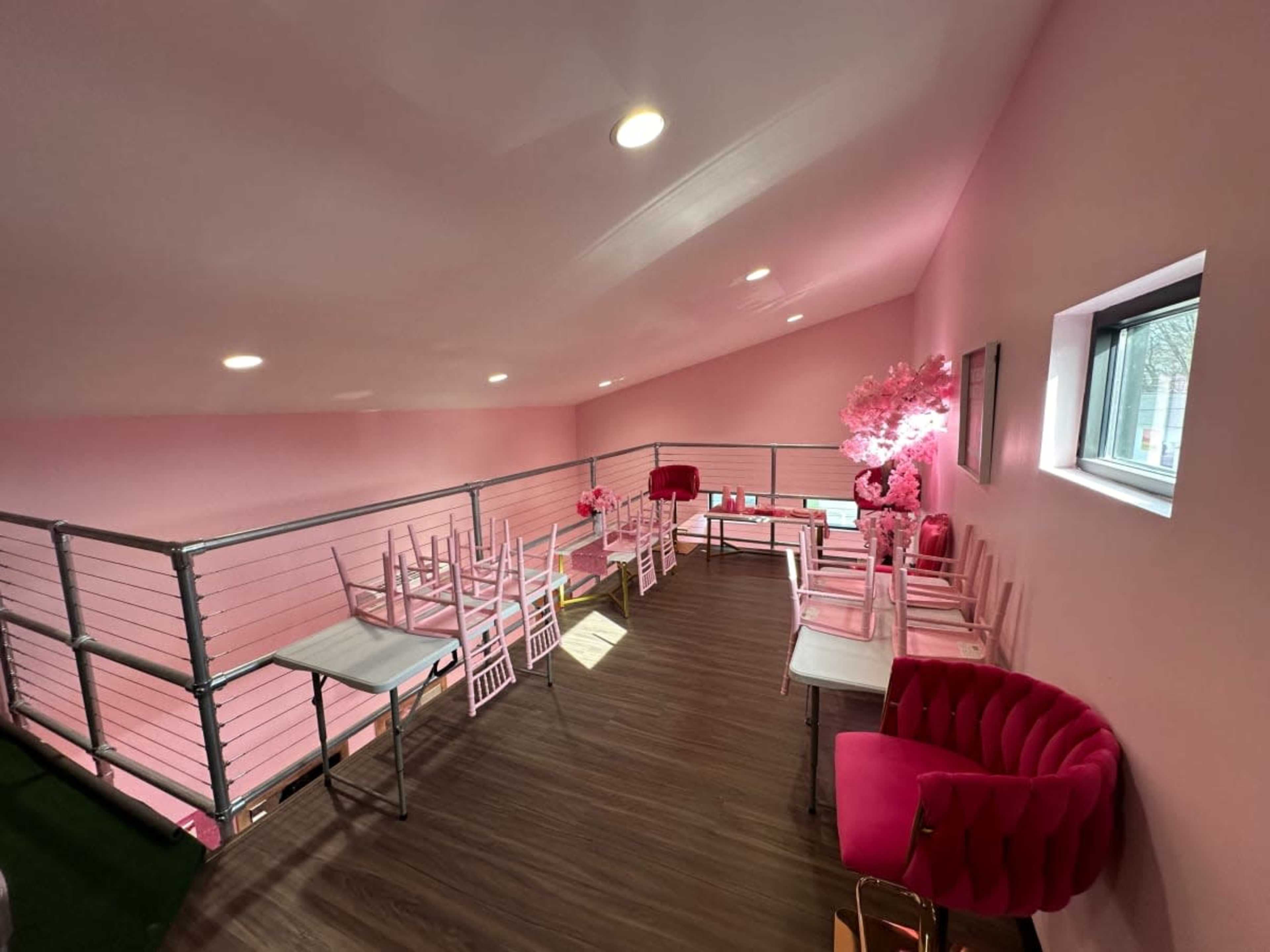 A brightly lit, pink-themed loft space with several chairs and tables, along with decorative elements like a pink tree.