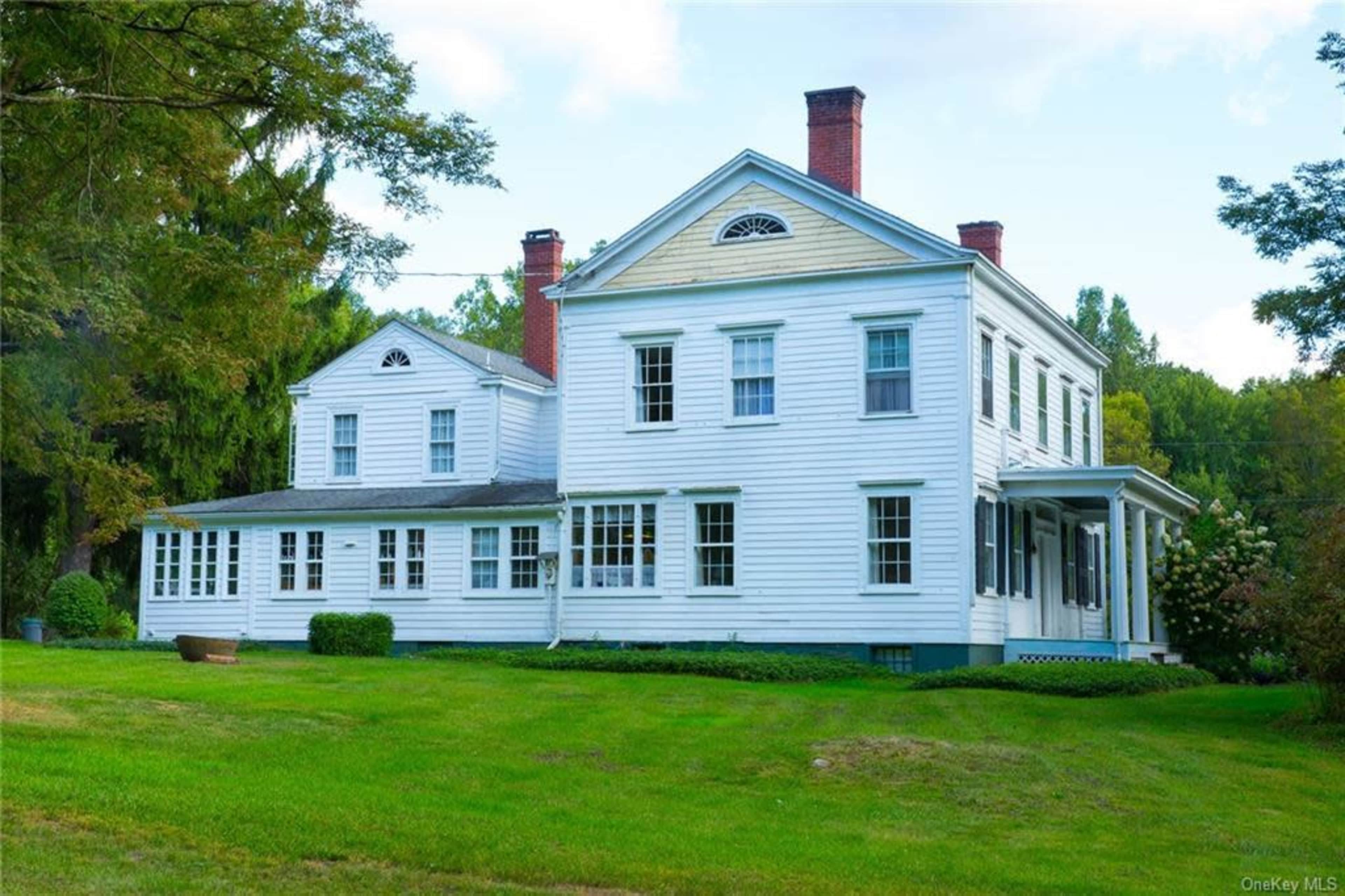 A two-story white colonial-style house with a large front porch and well-maintained lawn.