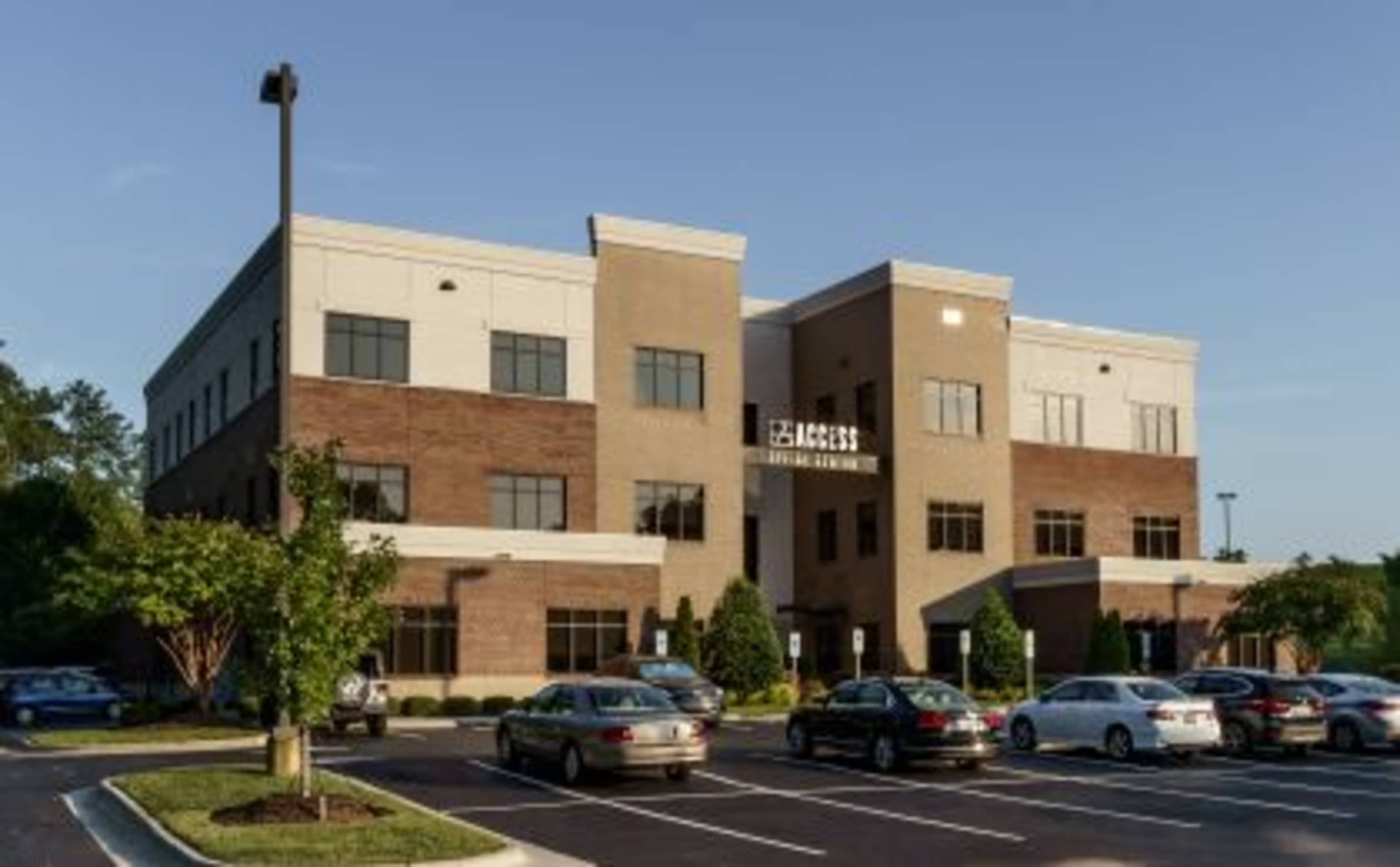 The image shows a multi-story commercial building with a brick and stucco exterior and a landscaped parking lot.