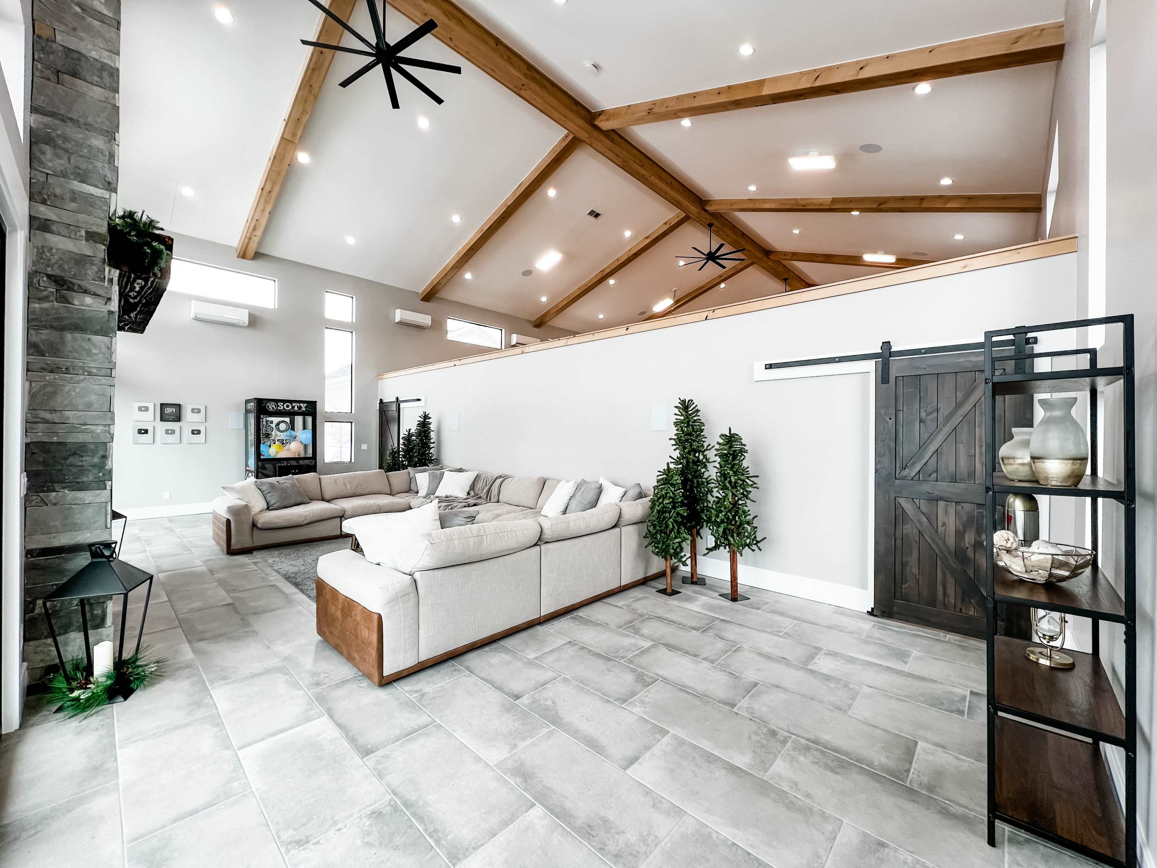 The spacious living area features a high ceiling with wooden beams, modern furniture, and large windows.