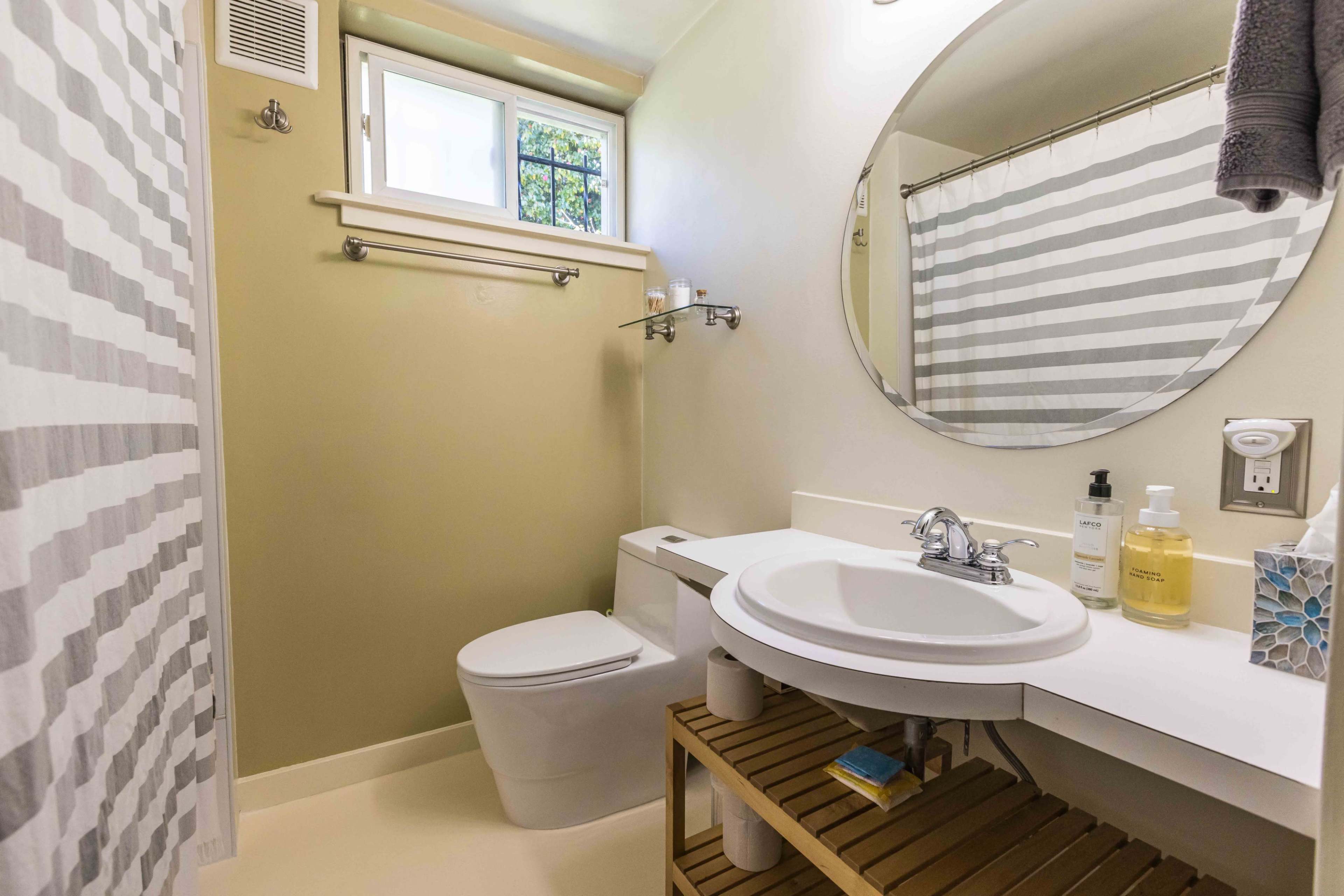 The image shows a bathroom with a toilet, a round mirror above a sink, and a striped shower curtain.