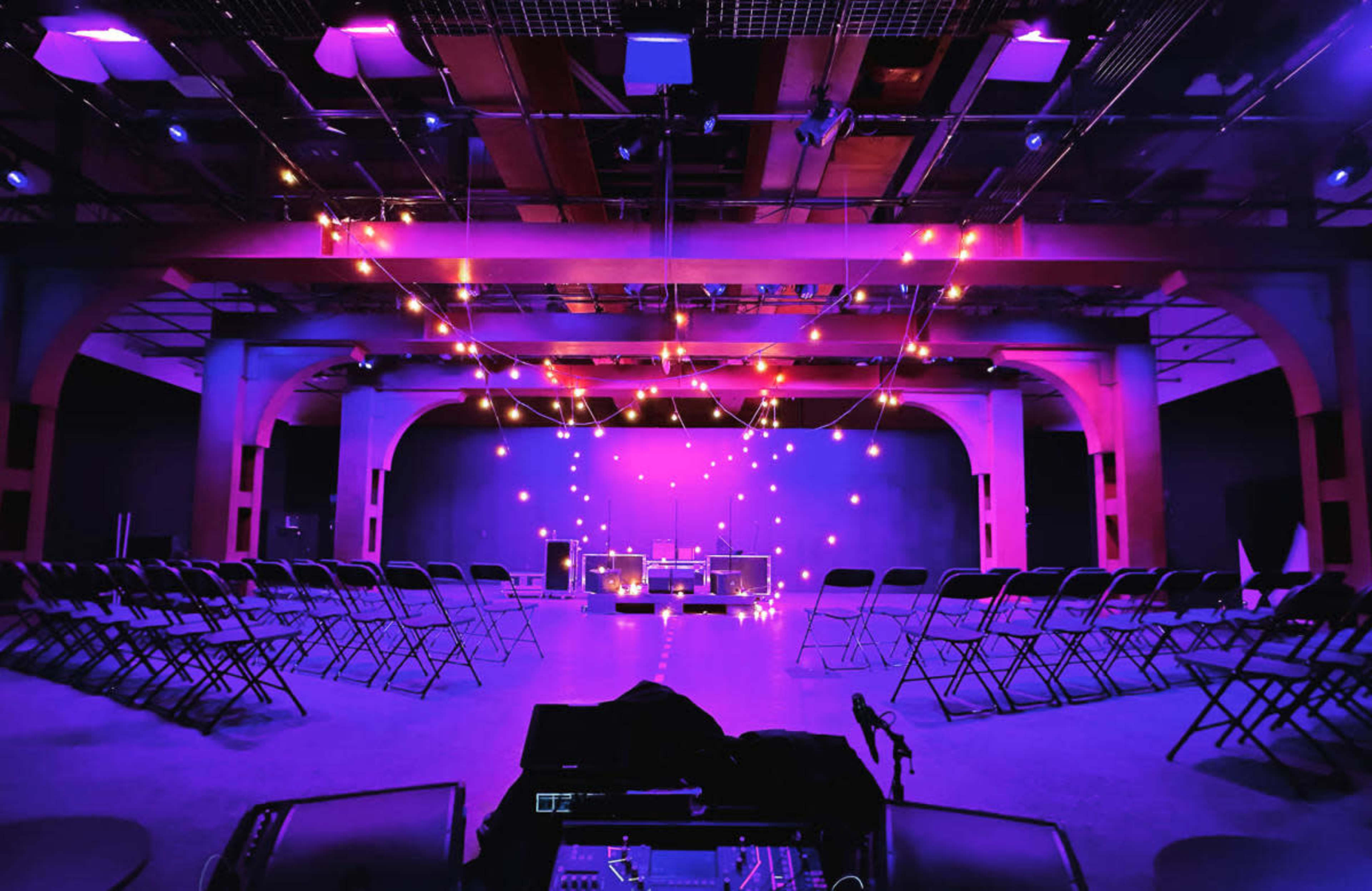 A dimly lit stage is set up with string lights and rows of chairs arranged in a circular layout.