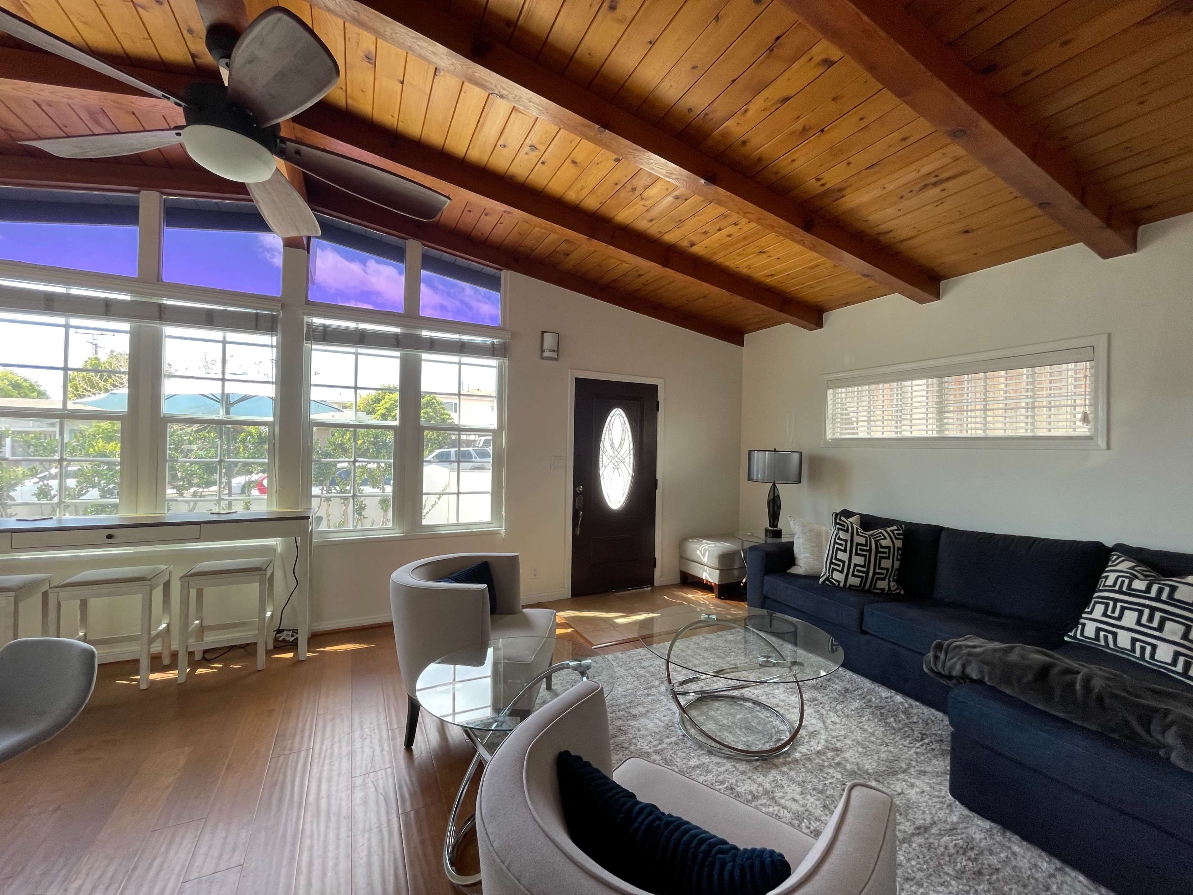 The living room features a dark couch, a glass coffee table, and large windows allowing natural light to enter.