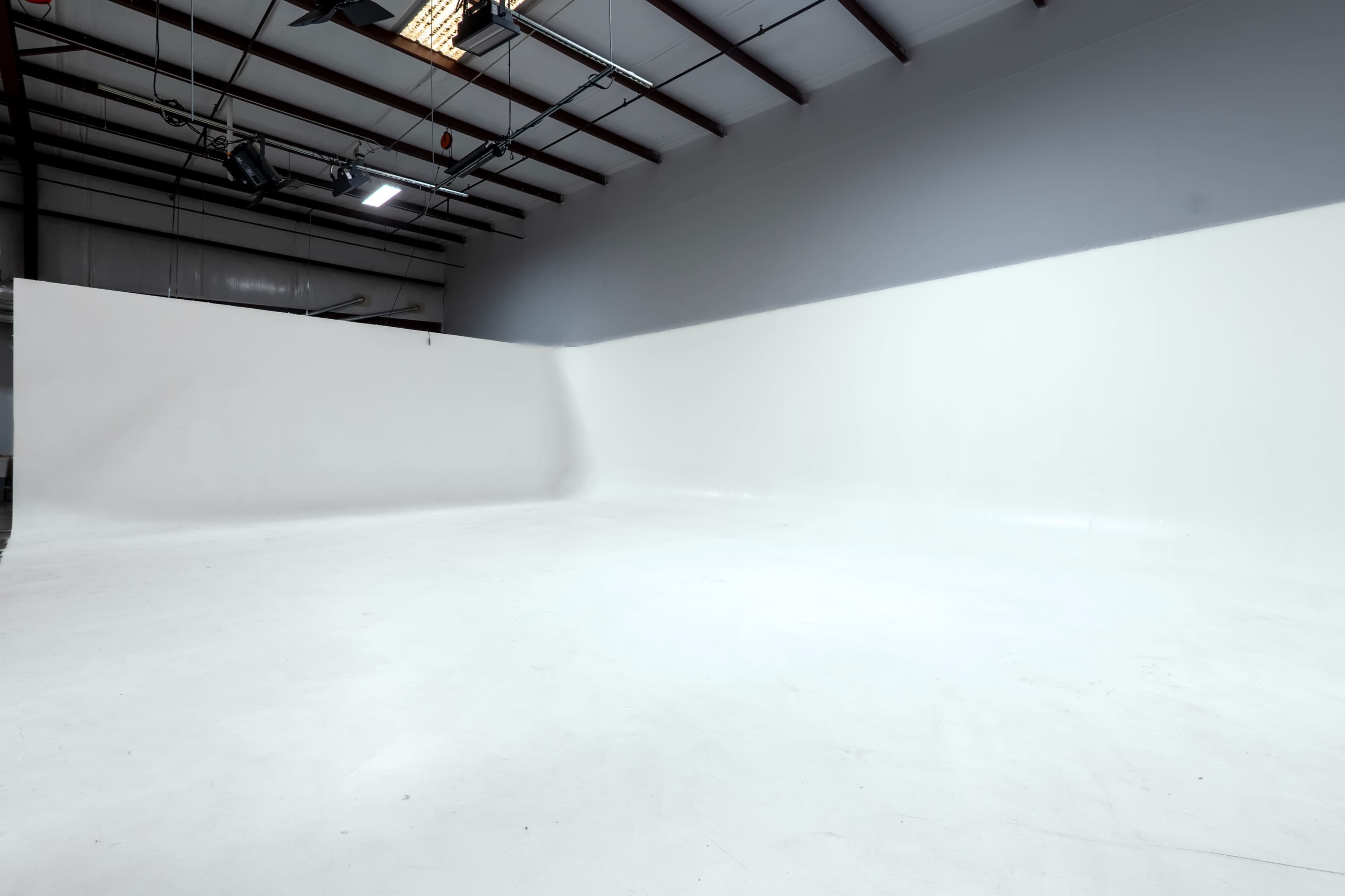 The image shows a large, empty studio space with white walls and a flat, white floor.