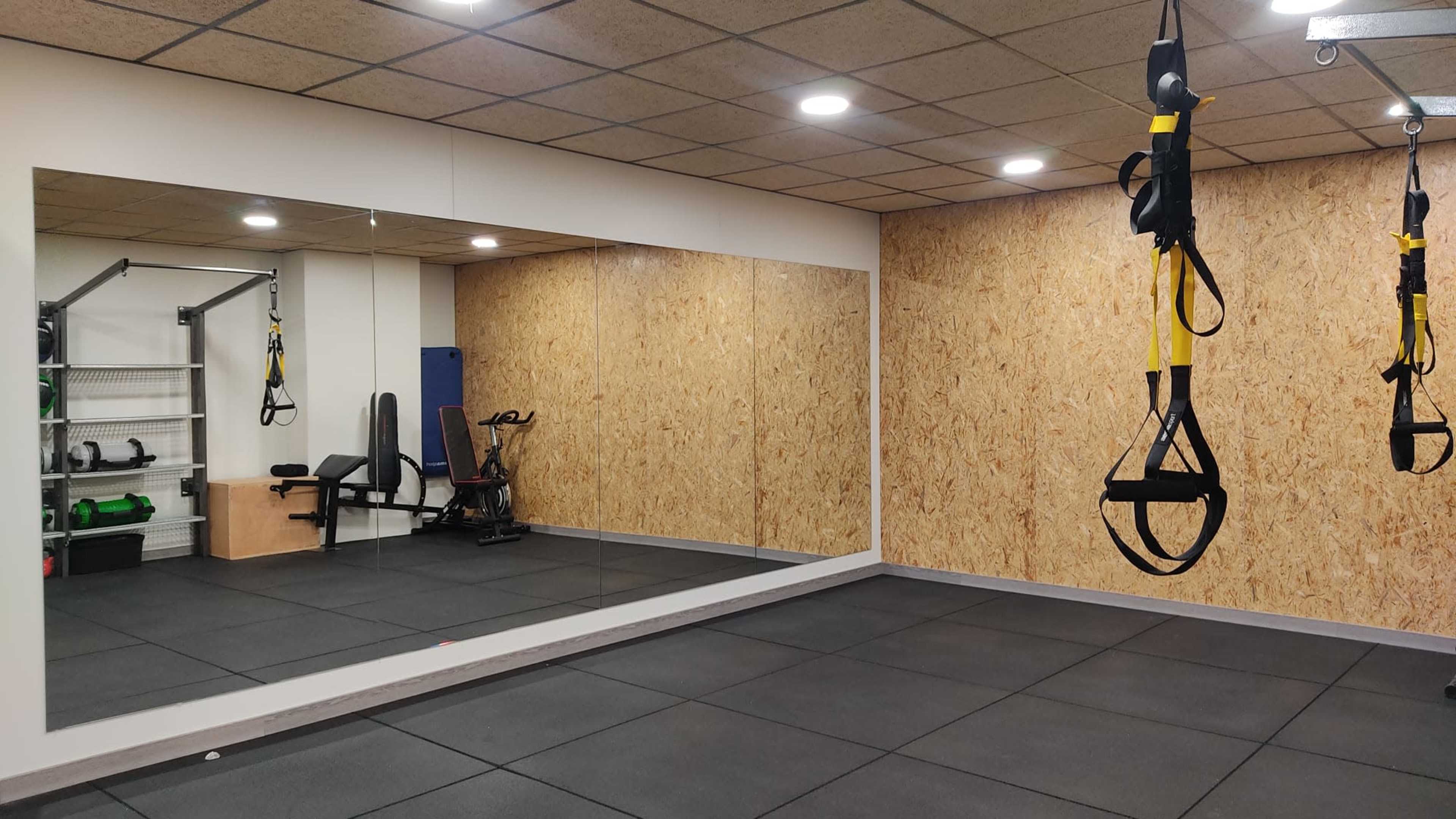 The image shows a gym space with a mirrored wall, workout equipment, and suspension training straps hanging from the ceiling.