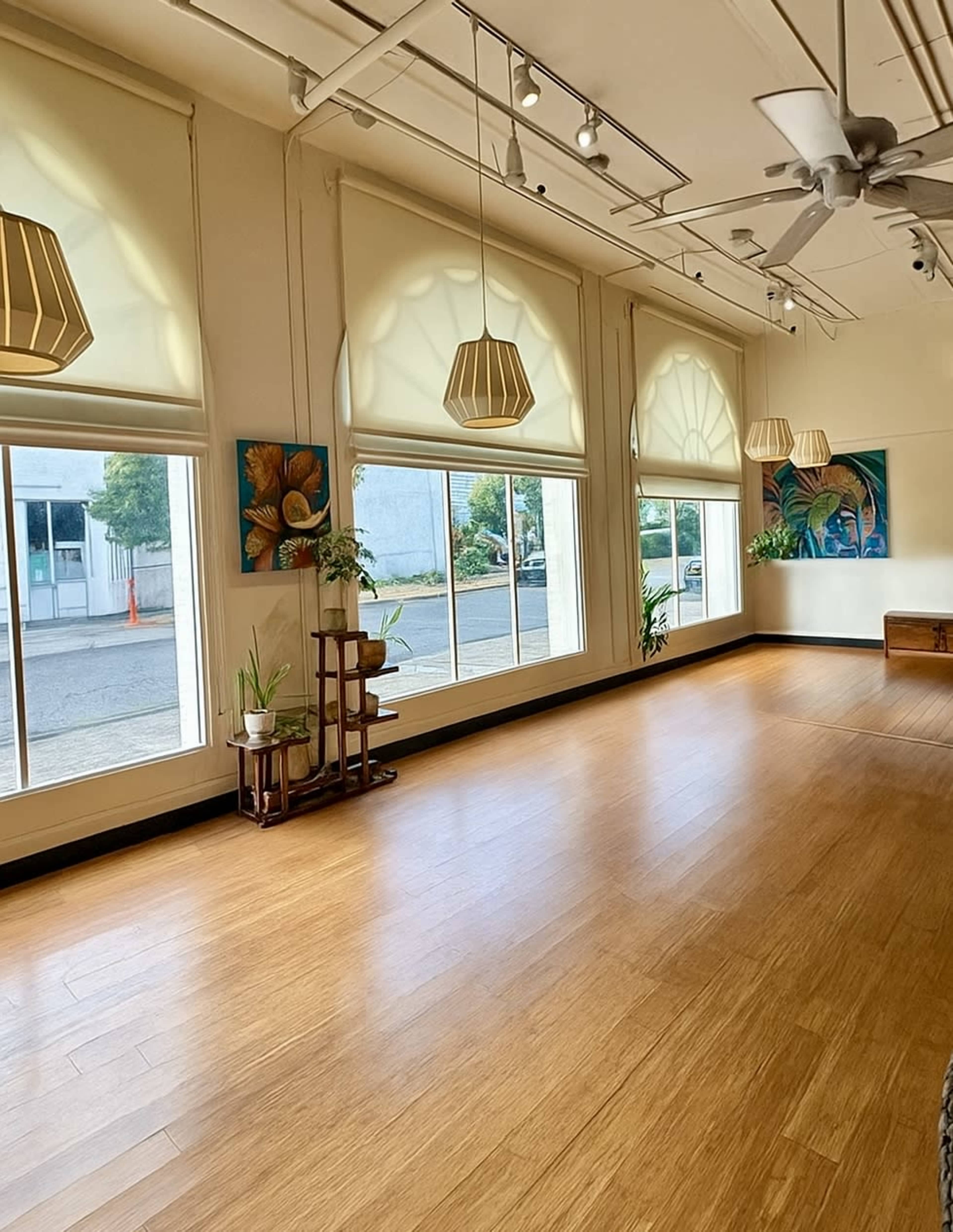 The image shows a spacious, well-lit room with large windows, wooden flooring, and decorative art on the walls.