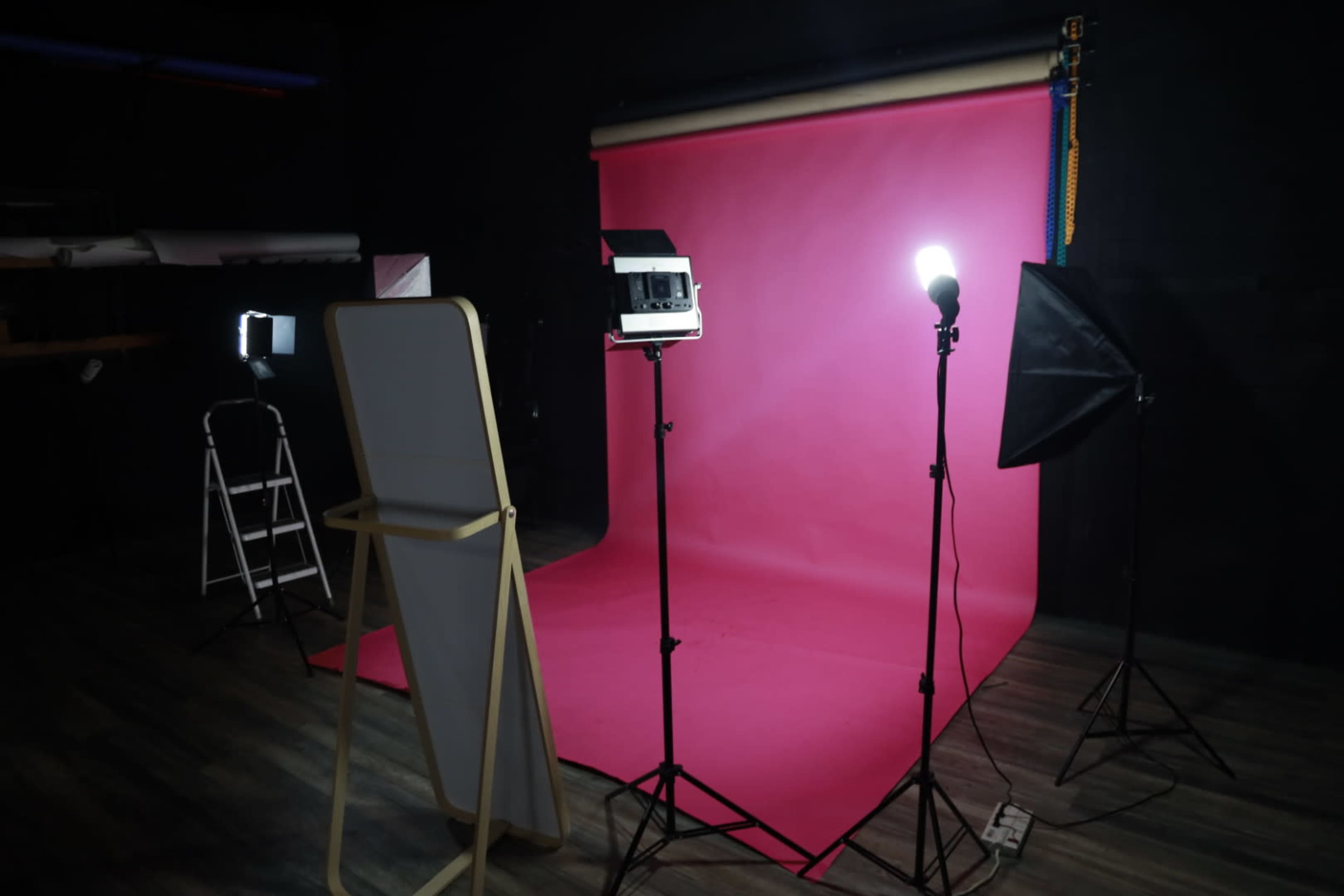 A photography studio is set up with a pink backdrop, lighting equipment, and a ladder.