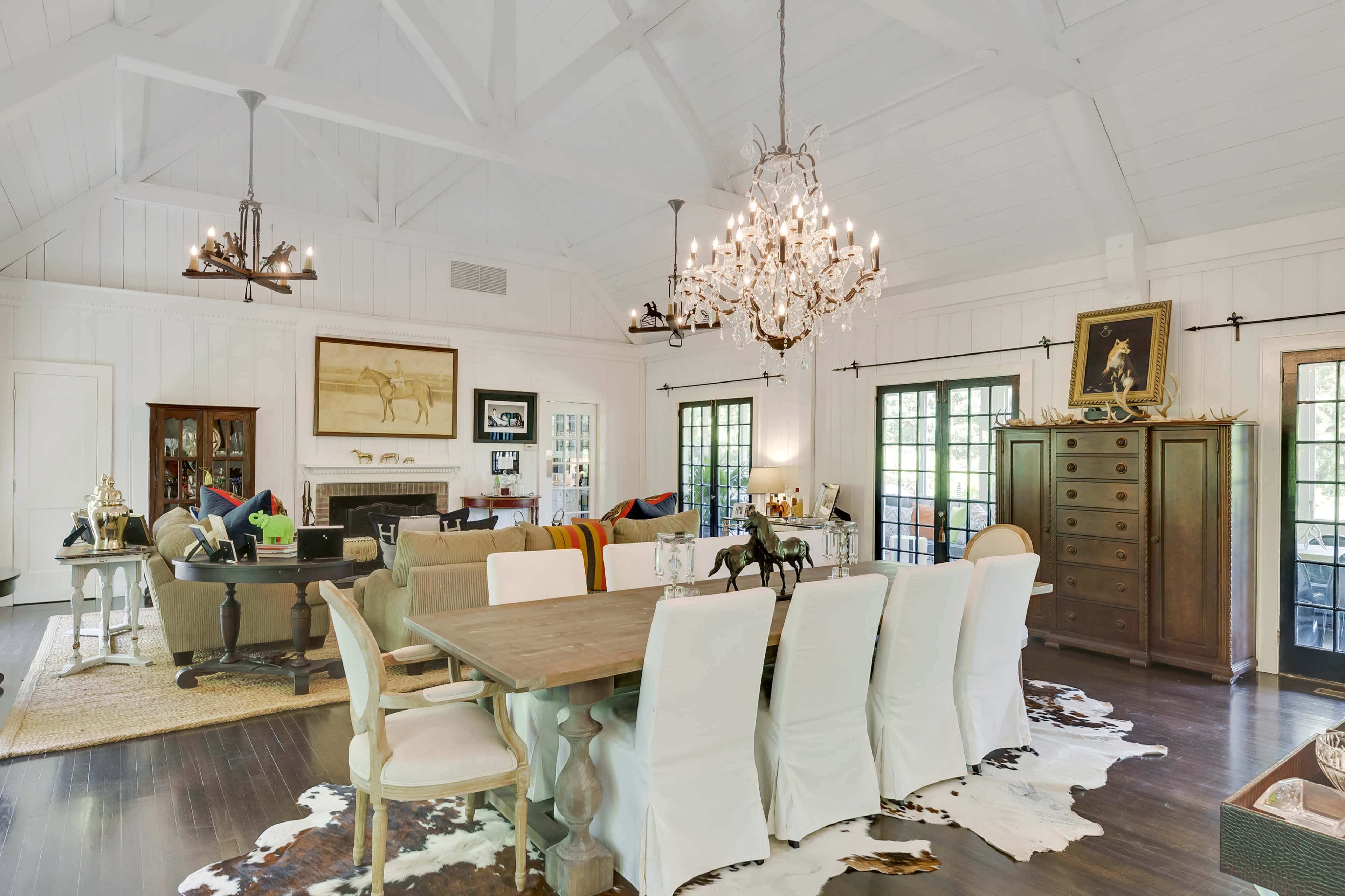 The image shows a spacious living and dining area featuring a chandelier, a large dining table, and a cozy seating arrangement with a fireplace.