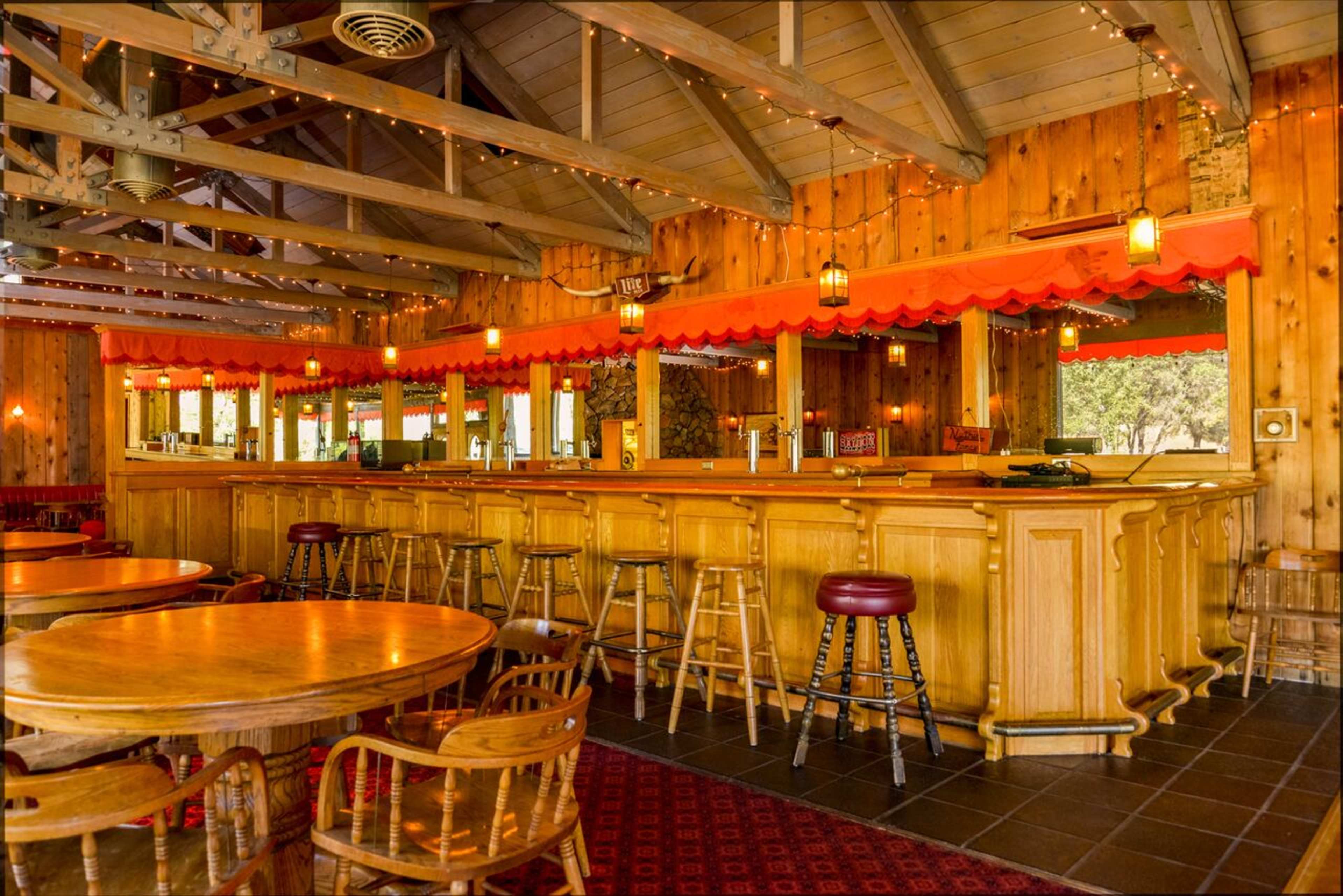 A wooden bar area with stools and tables, featuring warm lighting and rustic decor.