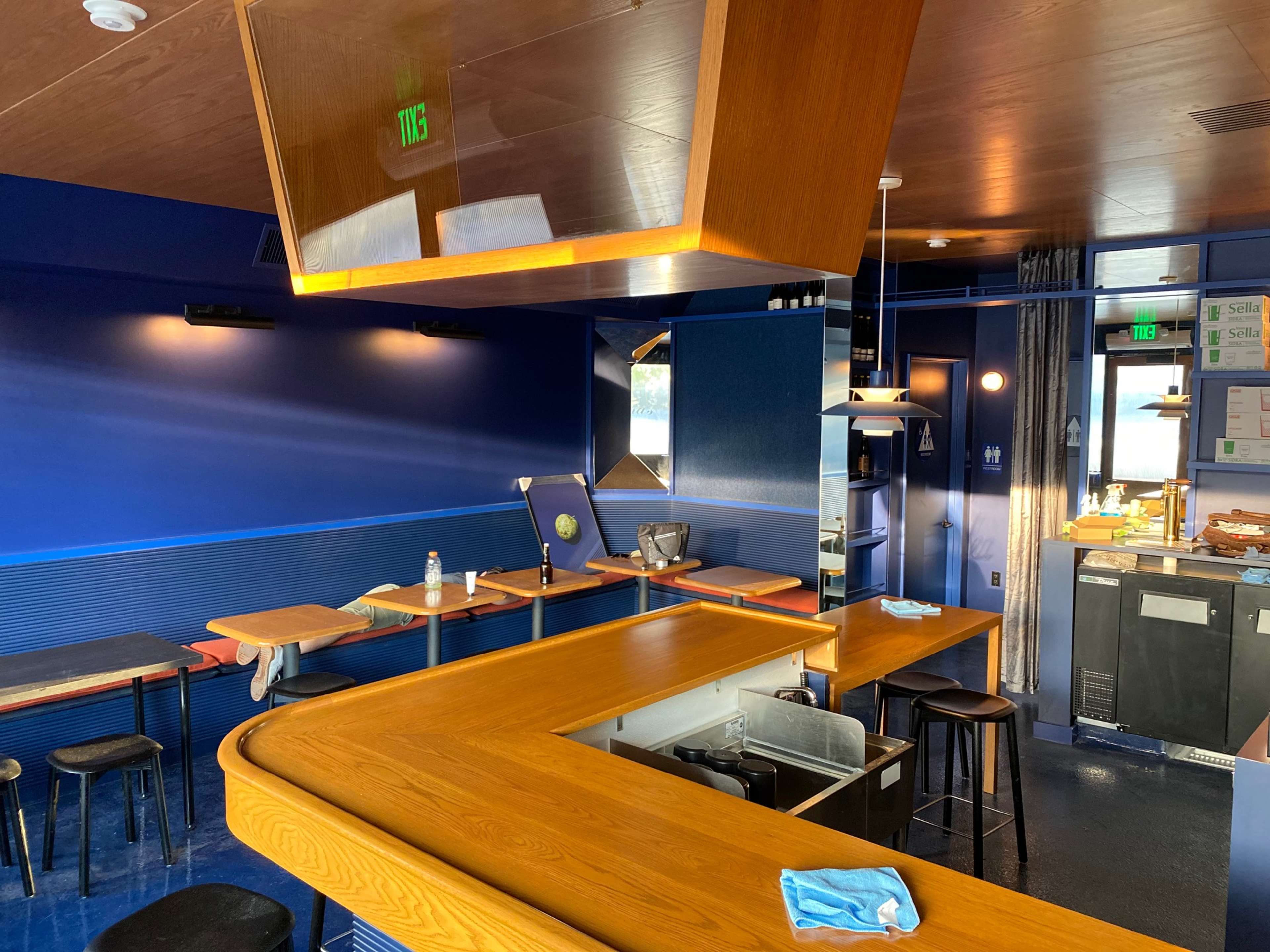 A modern cafe interior with a curved wooden counter, blue walls, and several small tables.