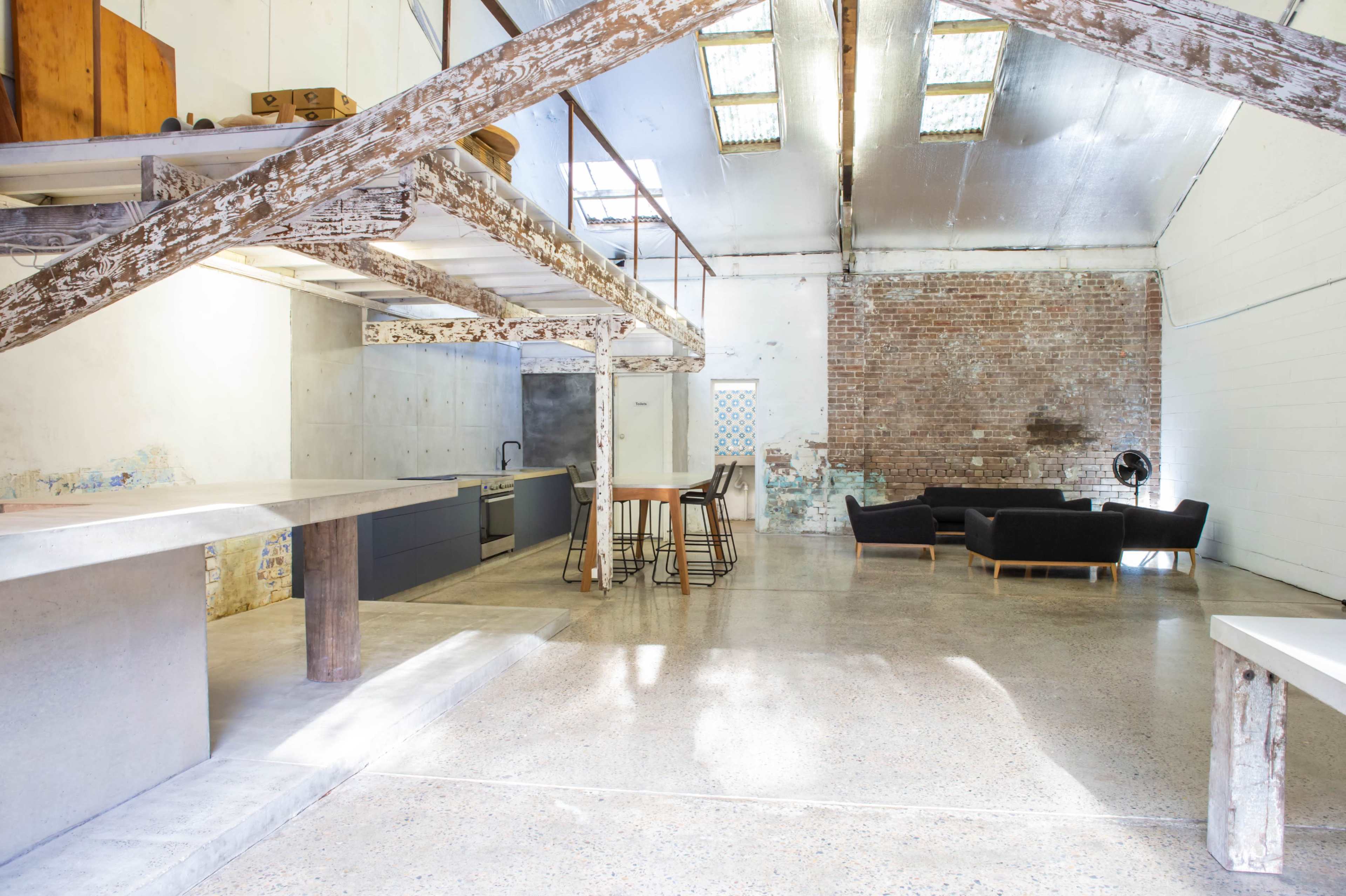 The image shows an open-concept loft space featuring a kitchen, dining area, and living room with exposed brick walls and wooden beams.