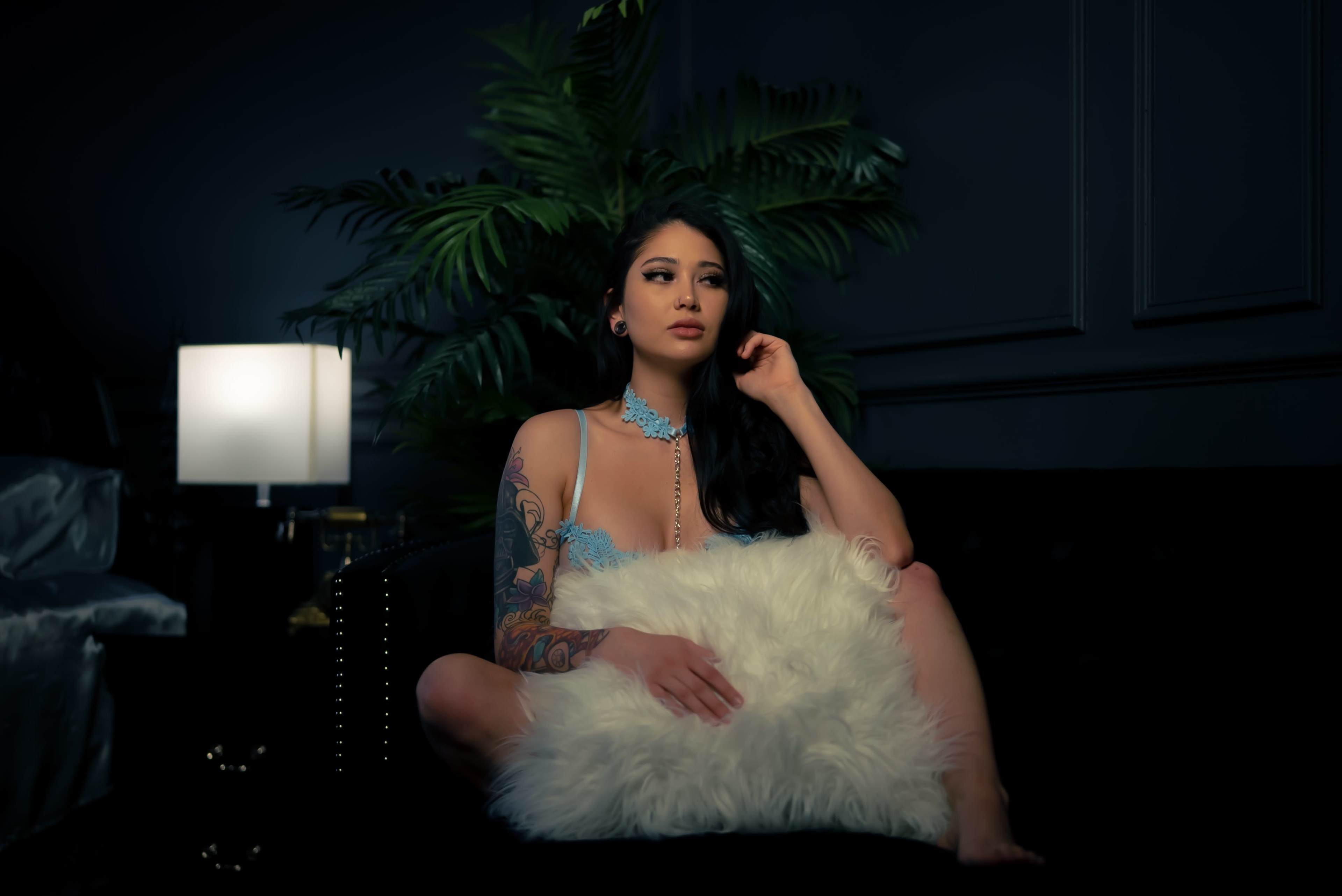 A person sits on a sofa holding a fluffy pillow, surrounded by indoor plants and soft lighting.