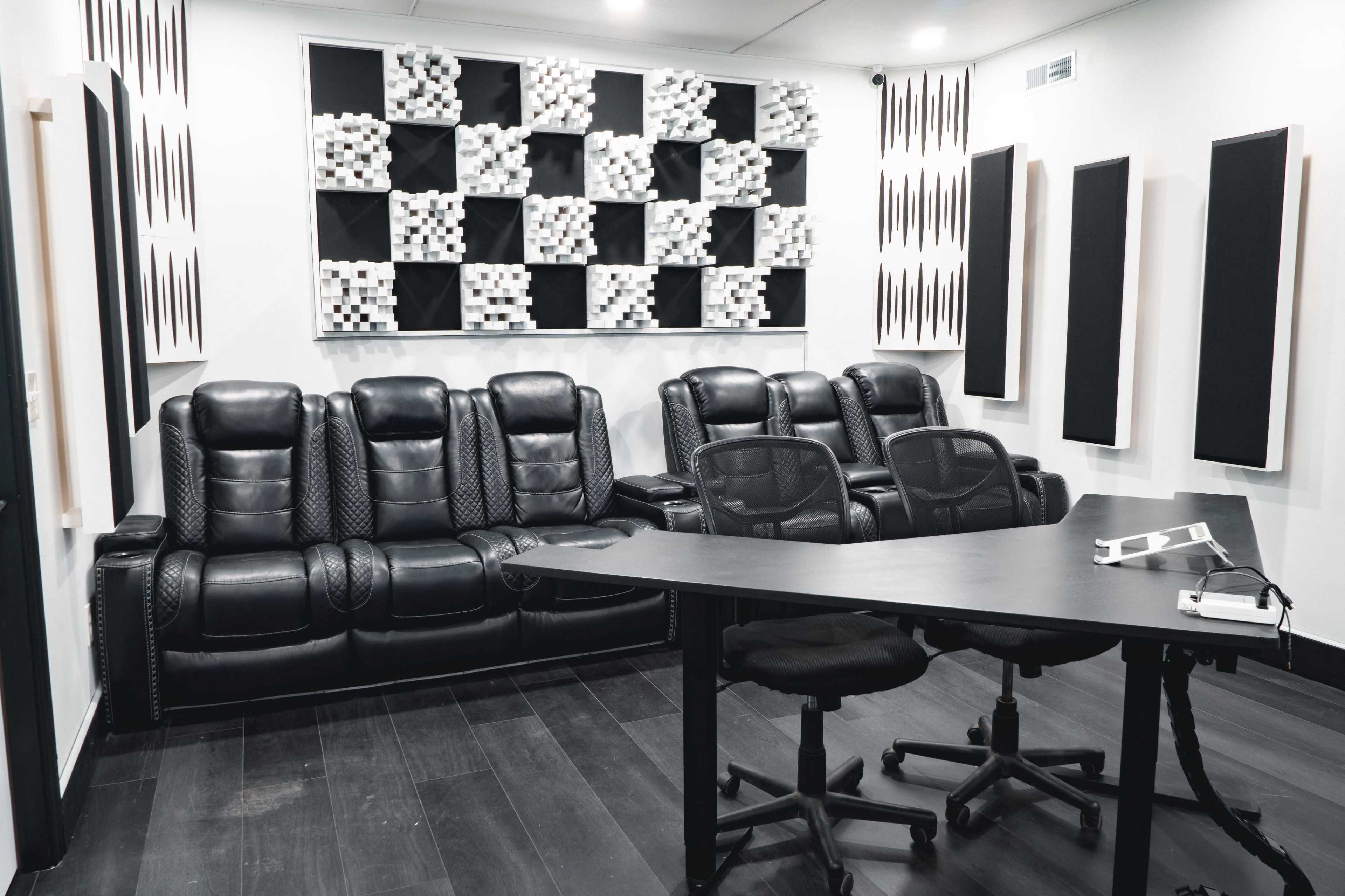 The image shows a modern audio studio featuring black leather seating, acoustic panels on the wall, and a desk with ergonomic chairs.