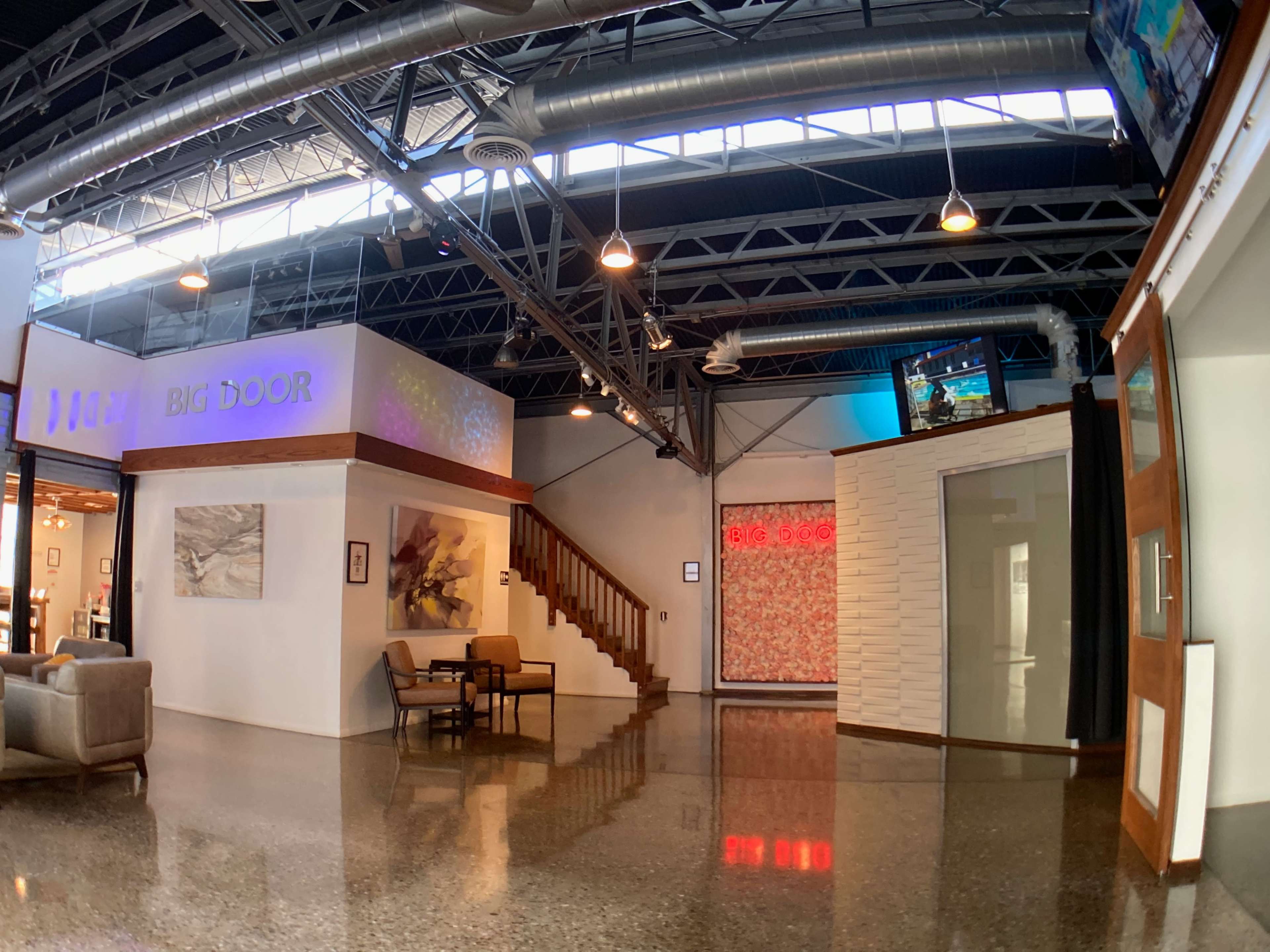 The image shows a modern interior space with polished concrete floors, a staircase, and walls featuring artwork and a large sign that reads "BIG DOOR."