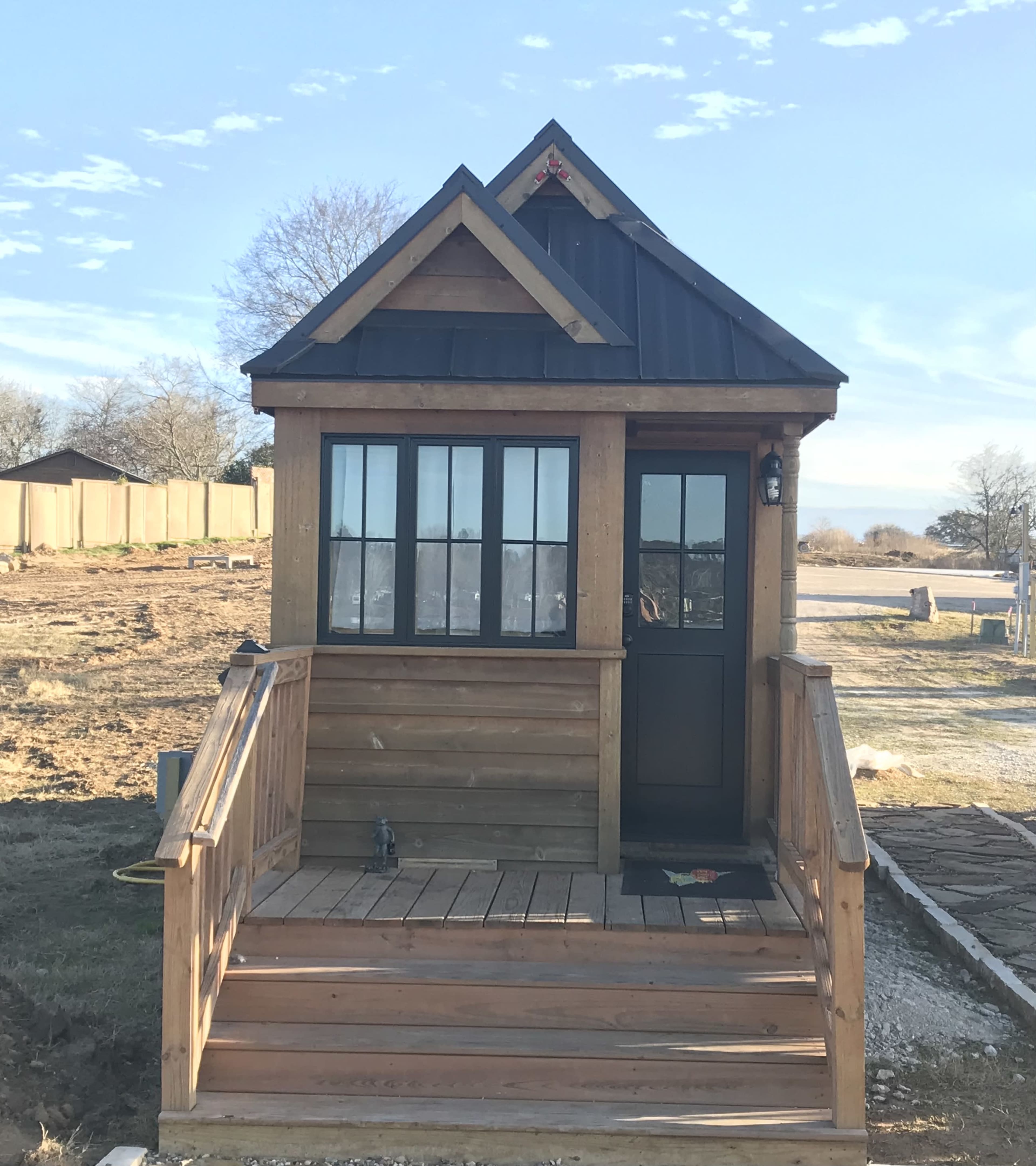 A small wooden cabin with a steep roof, a front porch, and a large window at the entrance.