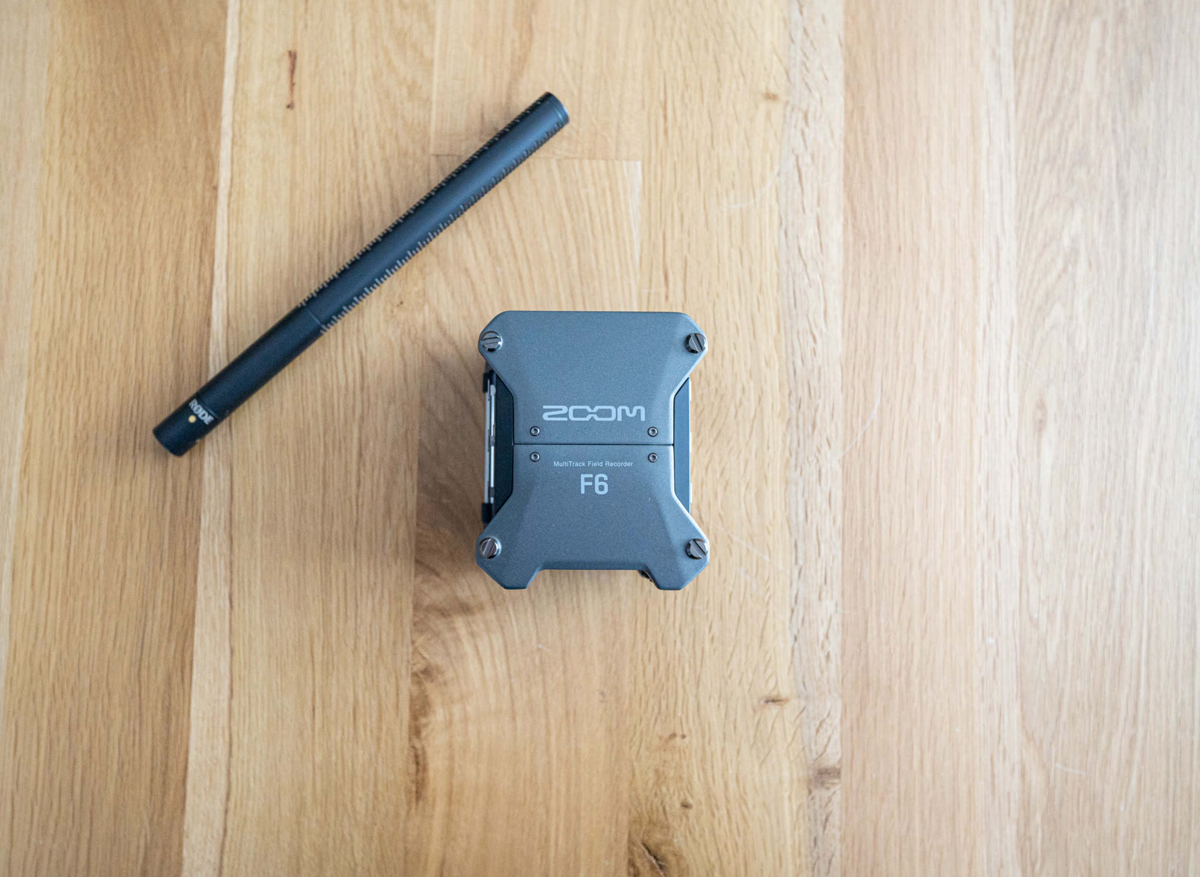 A Zoom F6 audio mixer placed on a wooden surface next to a black microphone.
