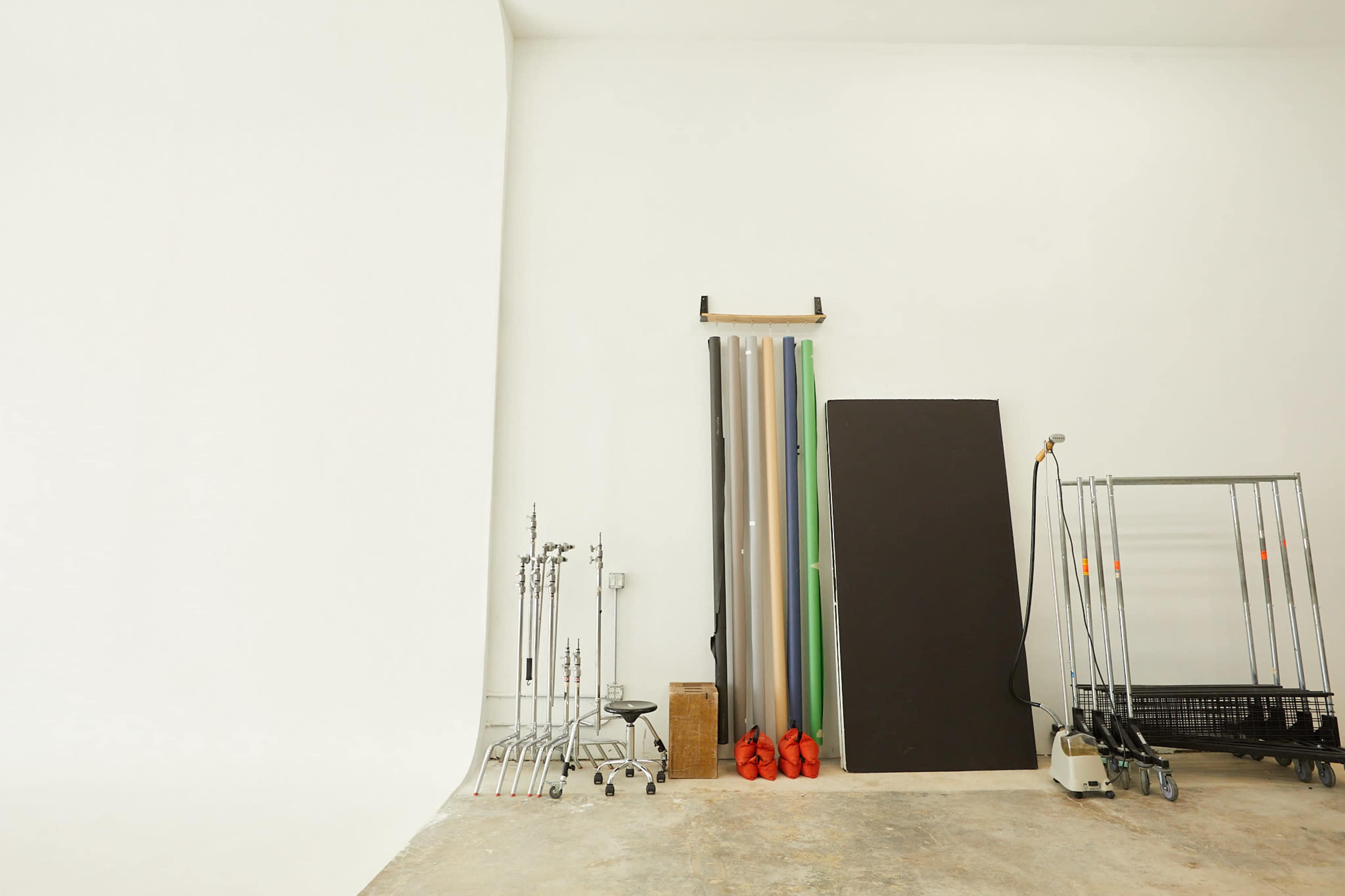 A photography studio with a seamless backdrop, various stands, and rolls of colored paper against a white wall.