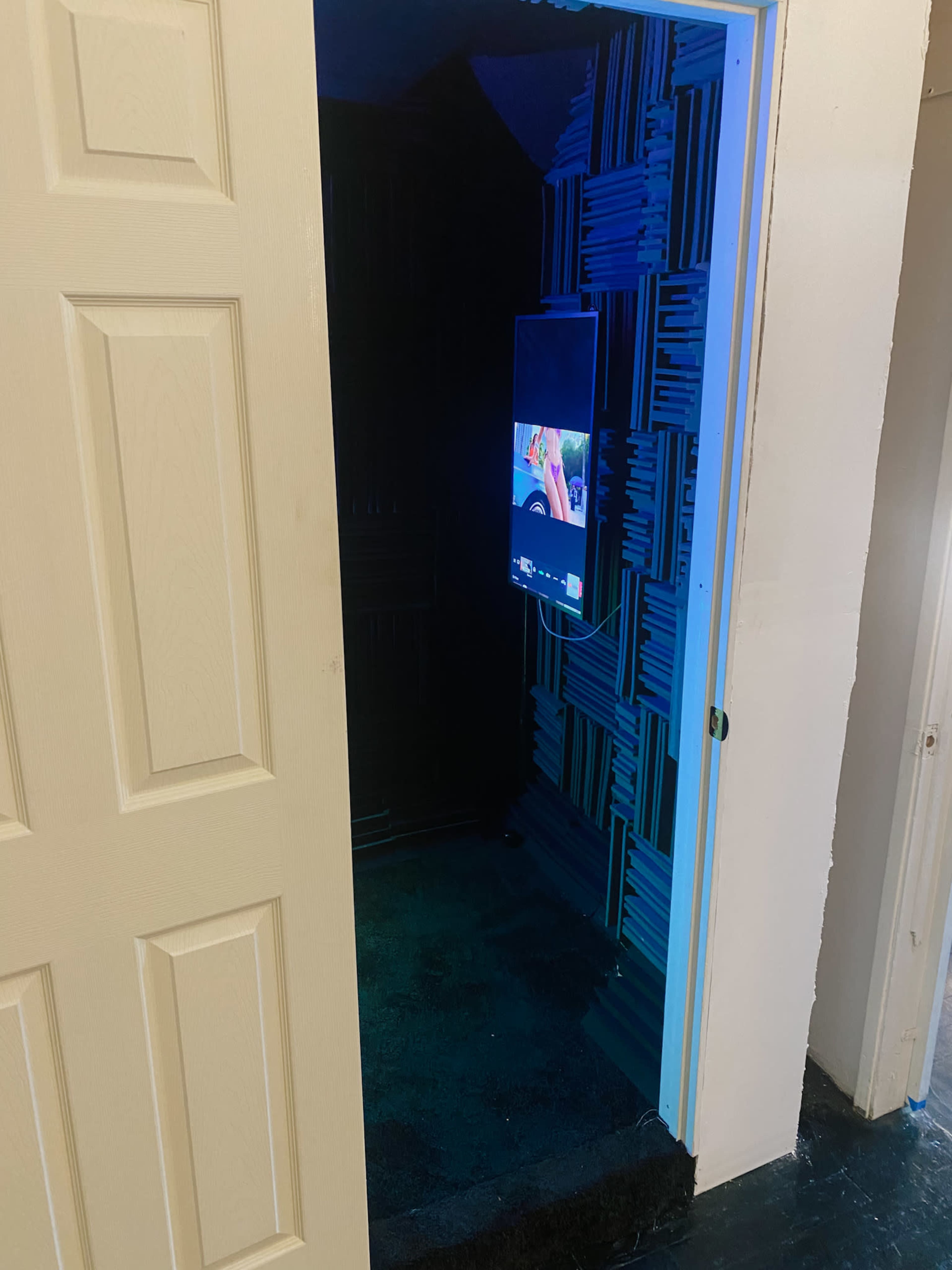 An open door leading to a room with acoustic paneling and a wall-mounted television.