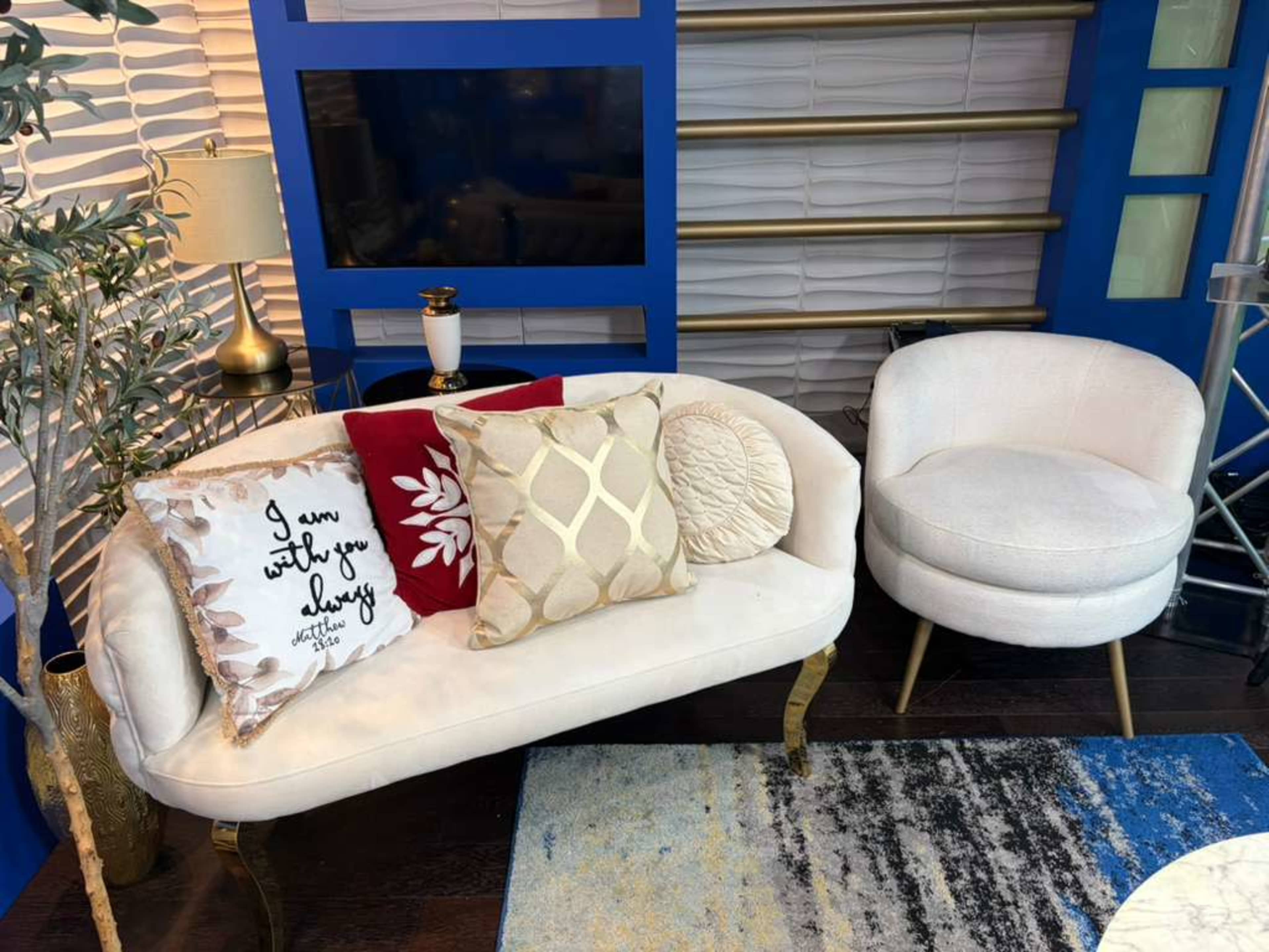 The image shows a stylish seating area featuring a white couch with decorative pillows and a round chair, set against a backdrop of blue and white decor.