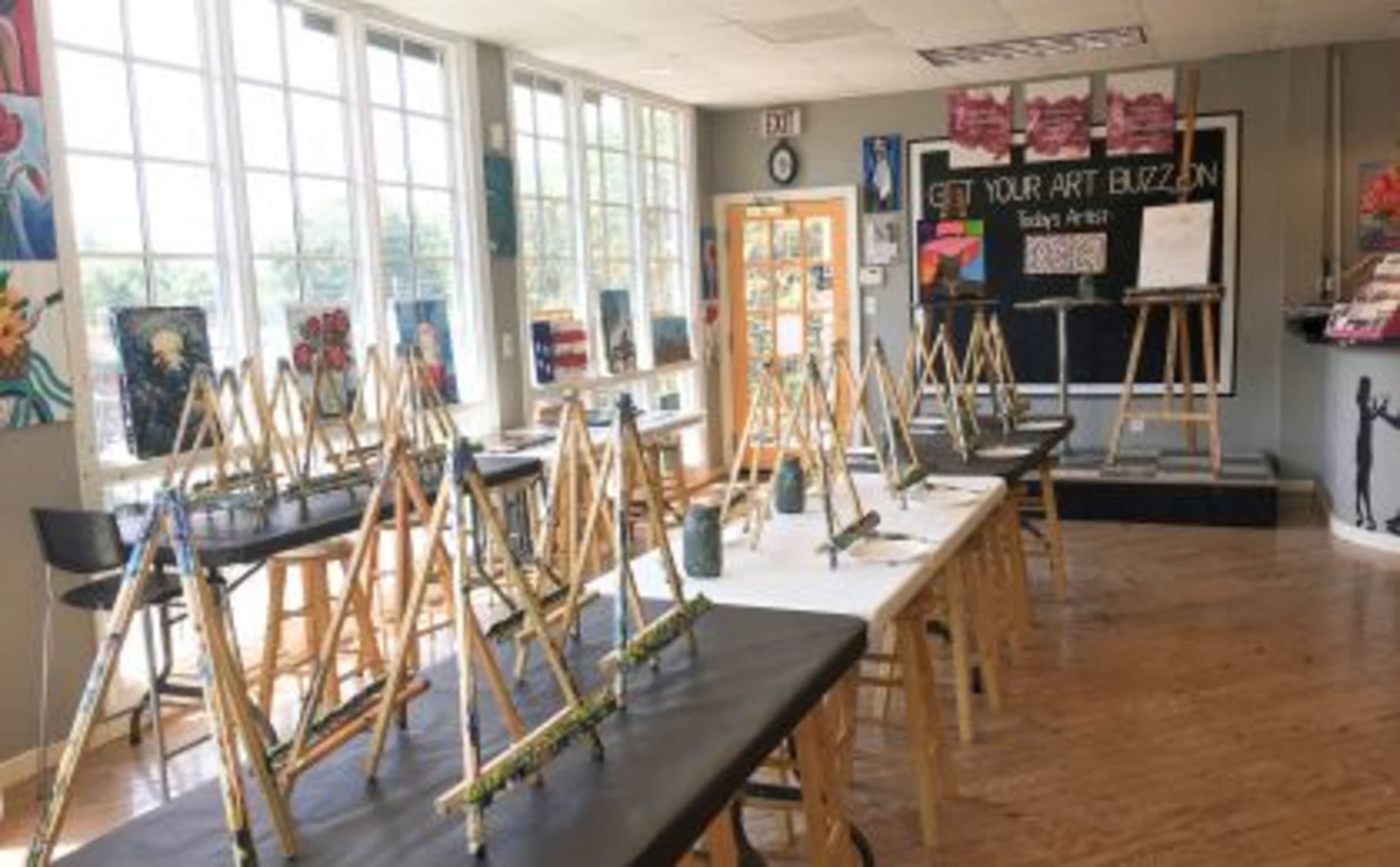 An art studio features several easels set up with canvases and paintbrushes arranged on tables.