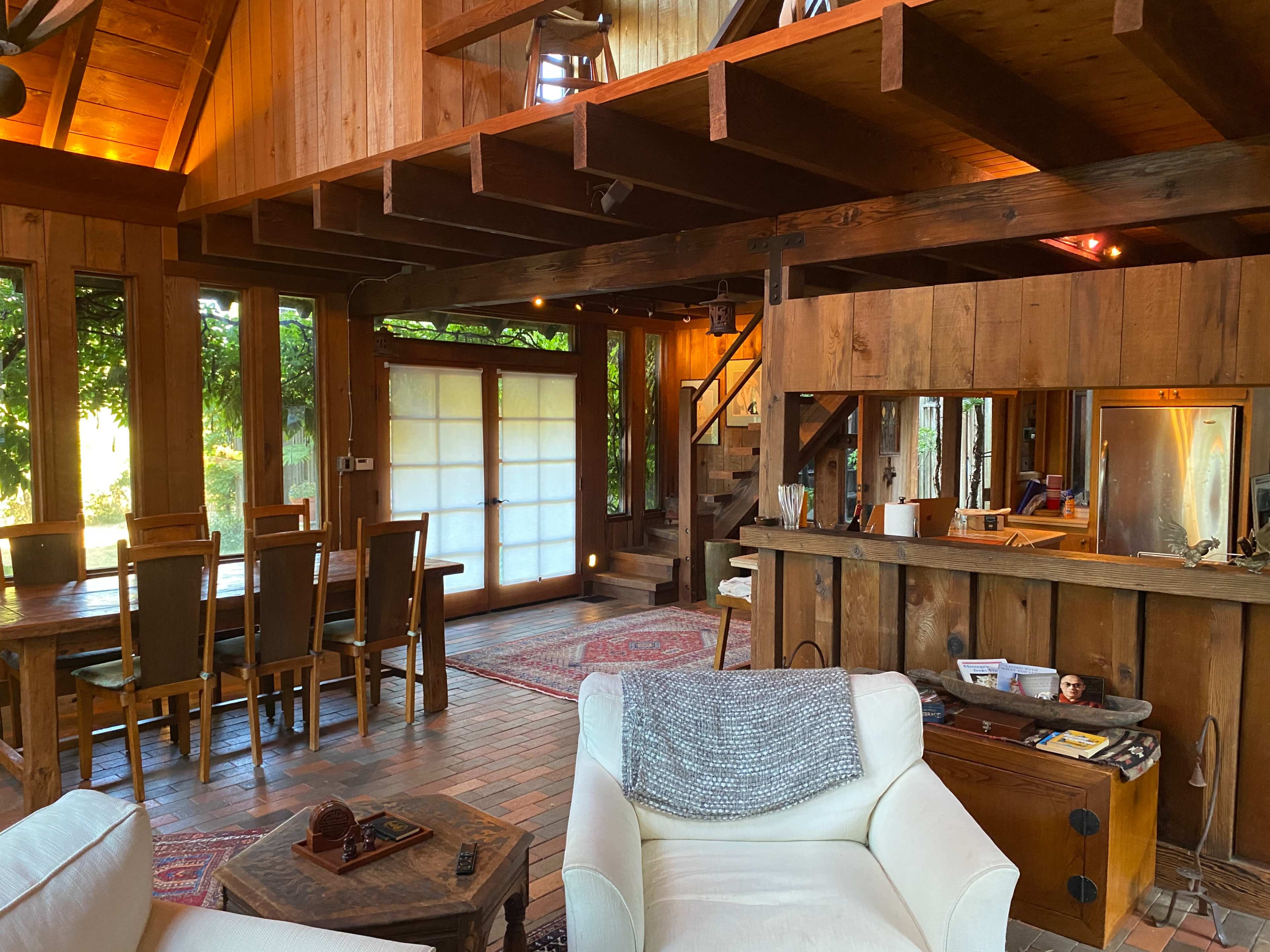 A wooden interior of a house with a dining area, a staircase, and an open living space featuring a sofa and a small table.