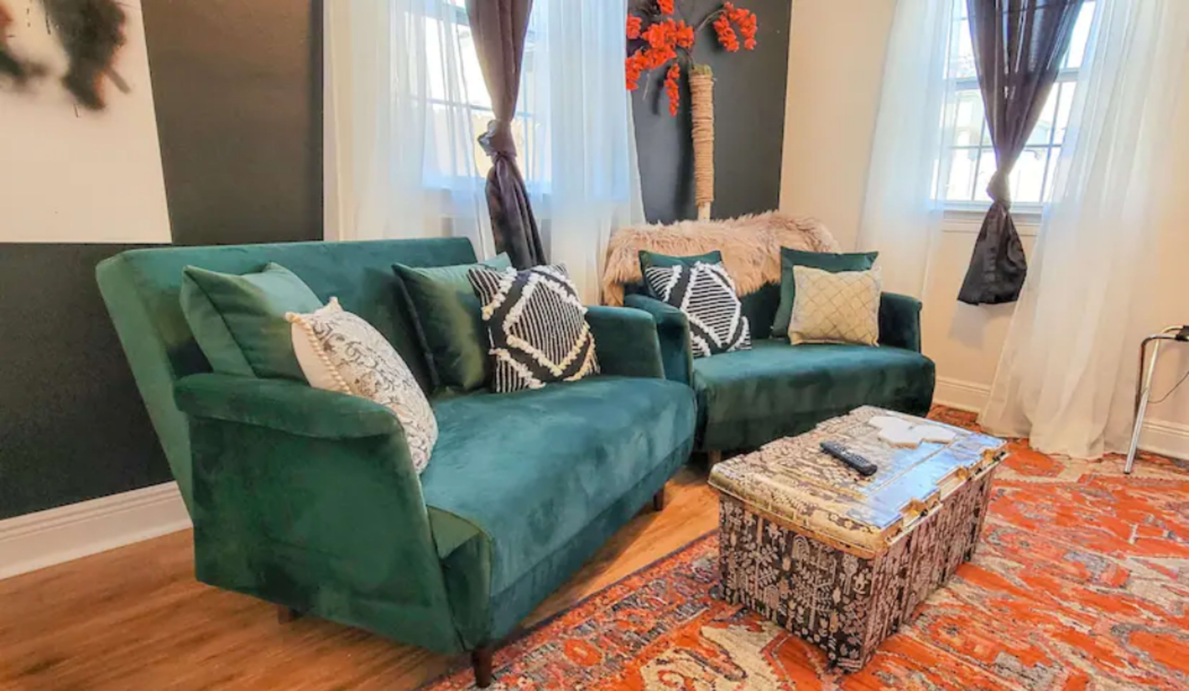 A living room with a green velvet sofa, decorative pillows, a patterned area rug, and a coffee table in front of the sofa.