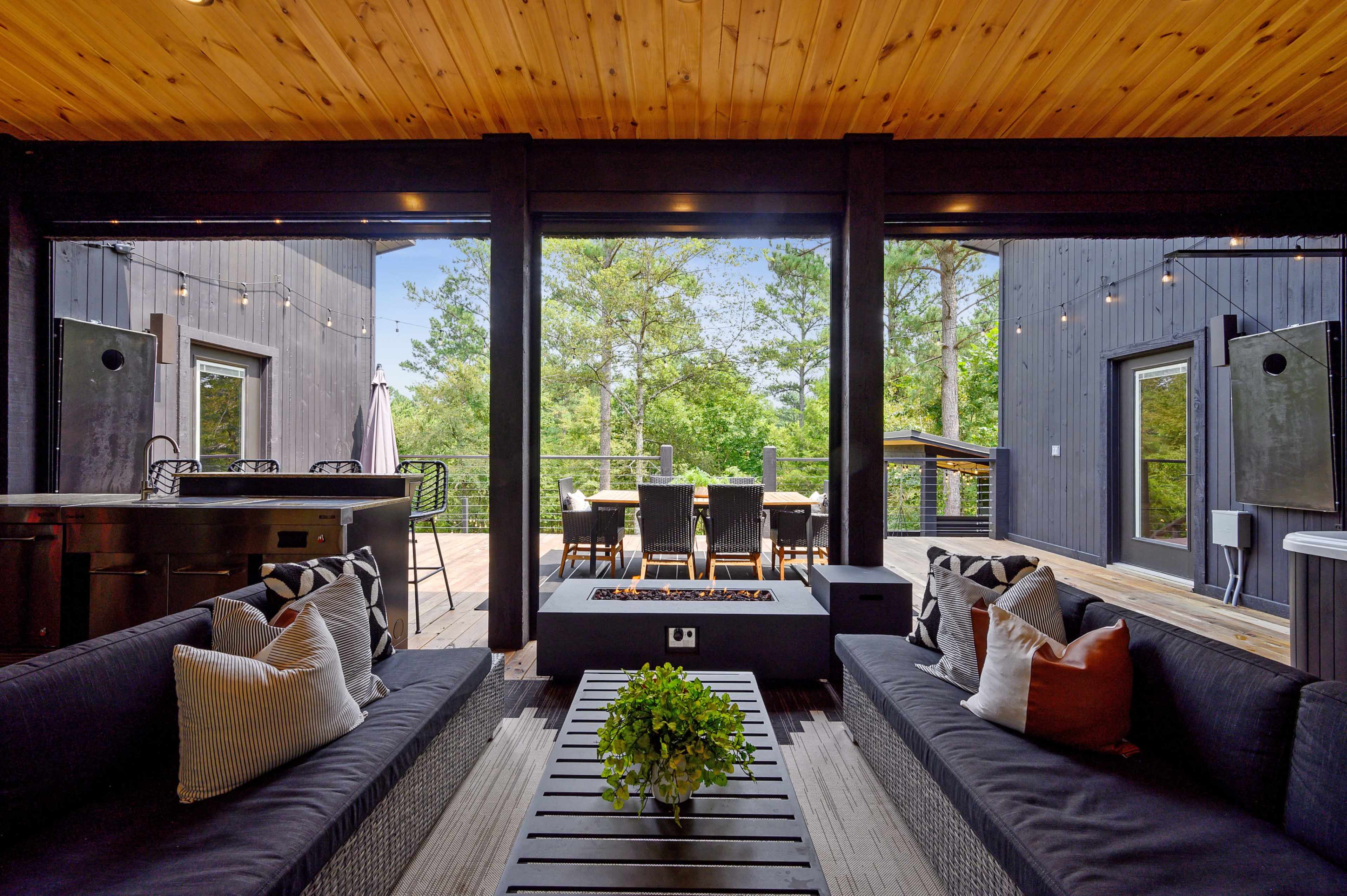 A modern outdoor living space with seating, a fire pit, and a dining area surrounded by trees.