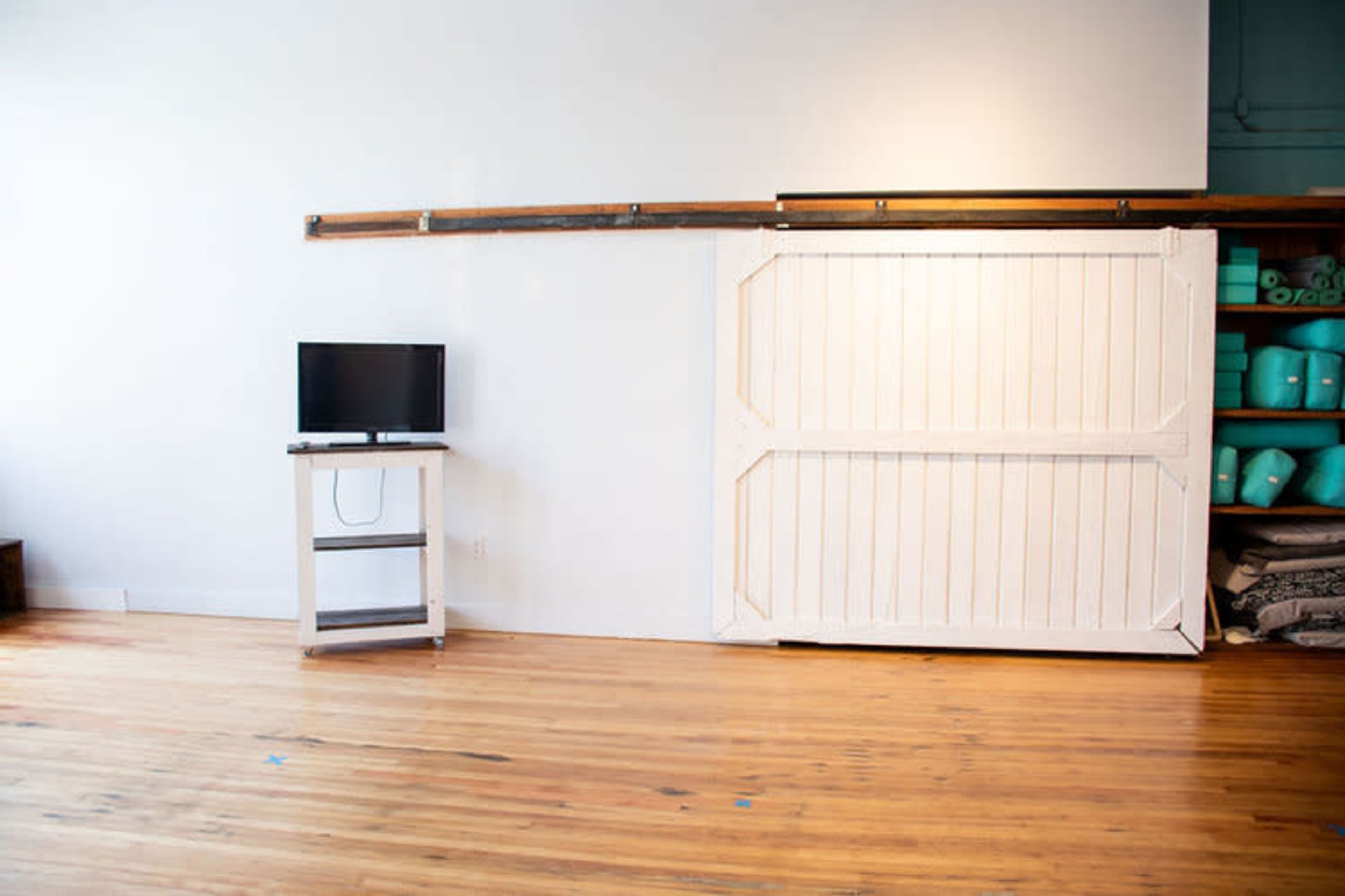 A simple interior space featuring a flat-screen TV on a white stand next to a large white sliding barn door on a wooden floor.
